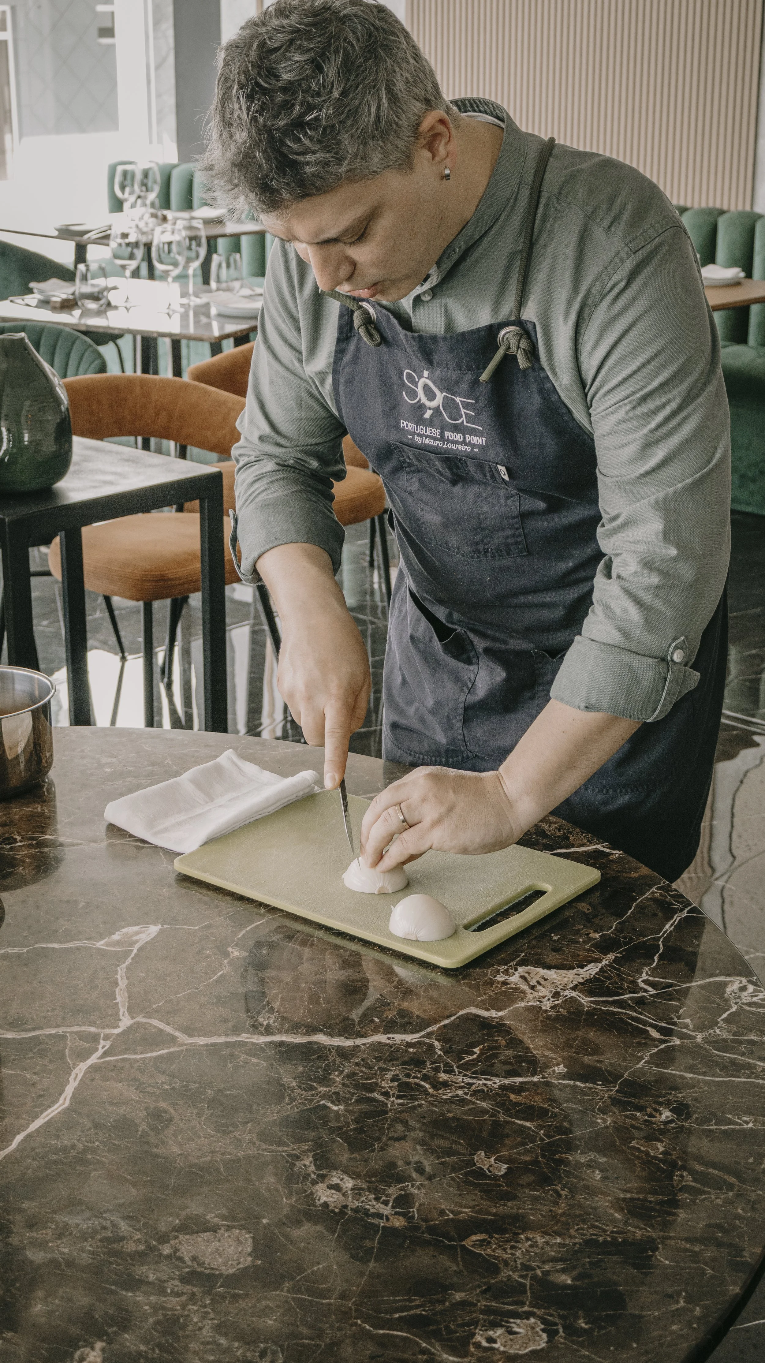 Pessoa preparando alimentos em uma cozinha, cortando cebolas ou similar em uma tábua de corte.