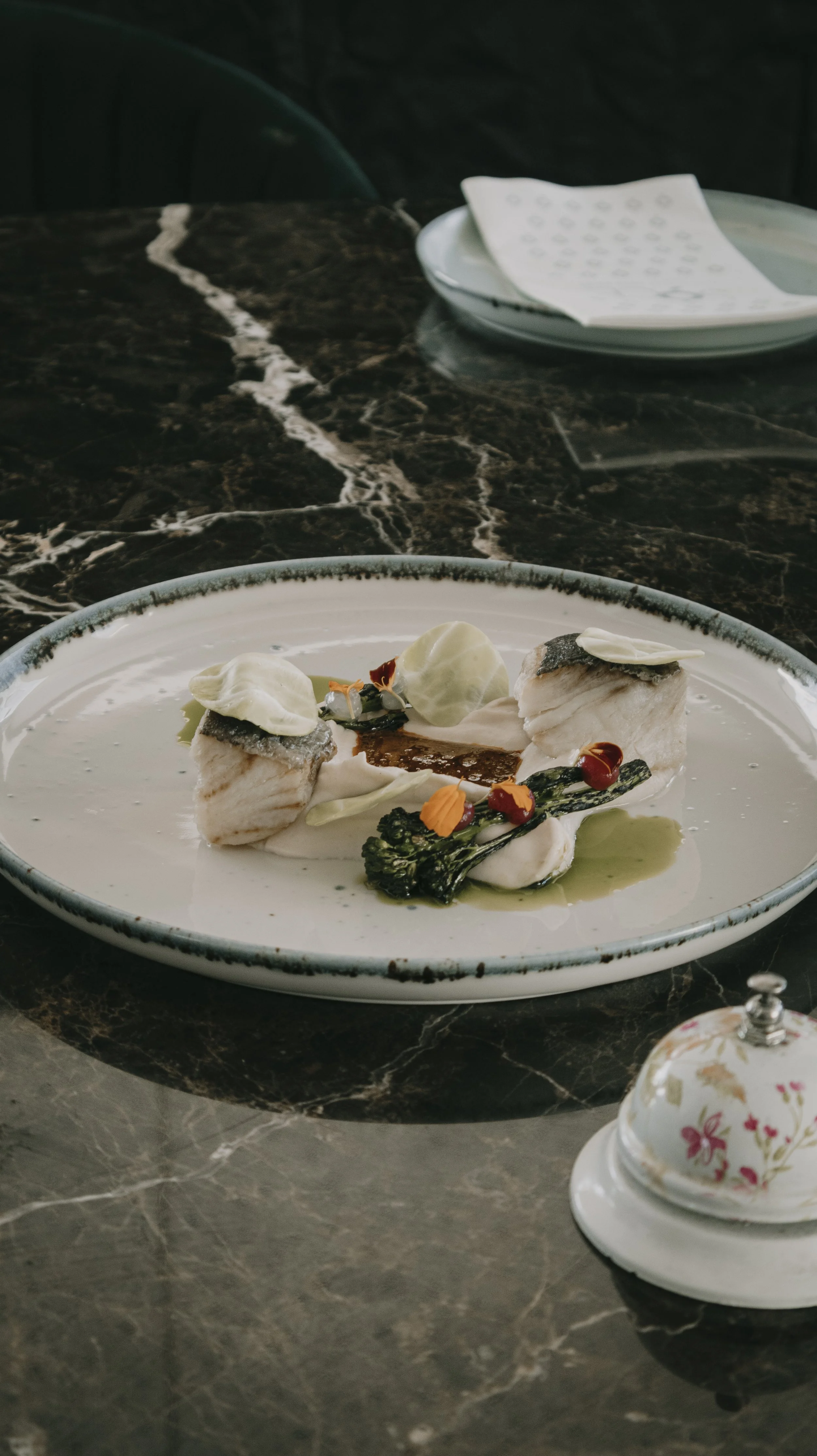 Prato de comida sofisticada com peixe, grelos, folhas e glórias na apresentação.”}