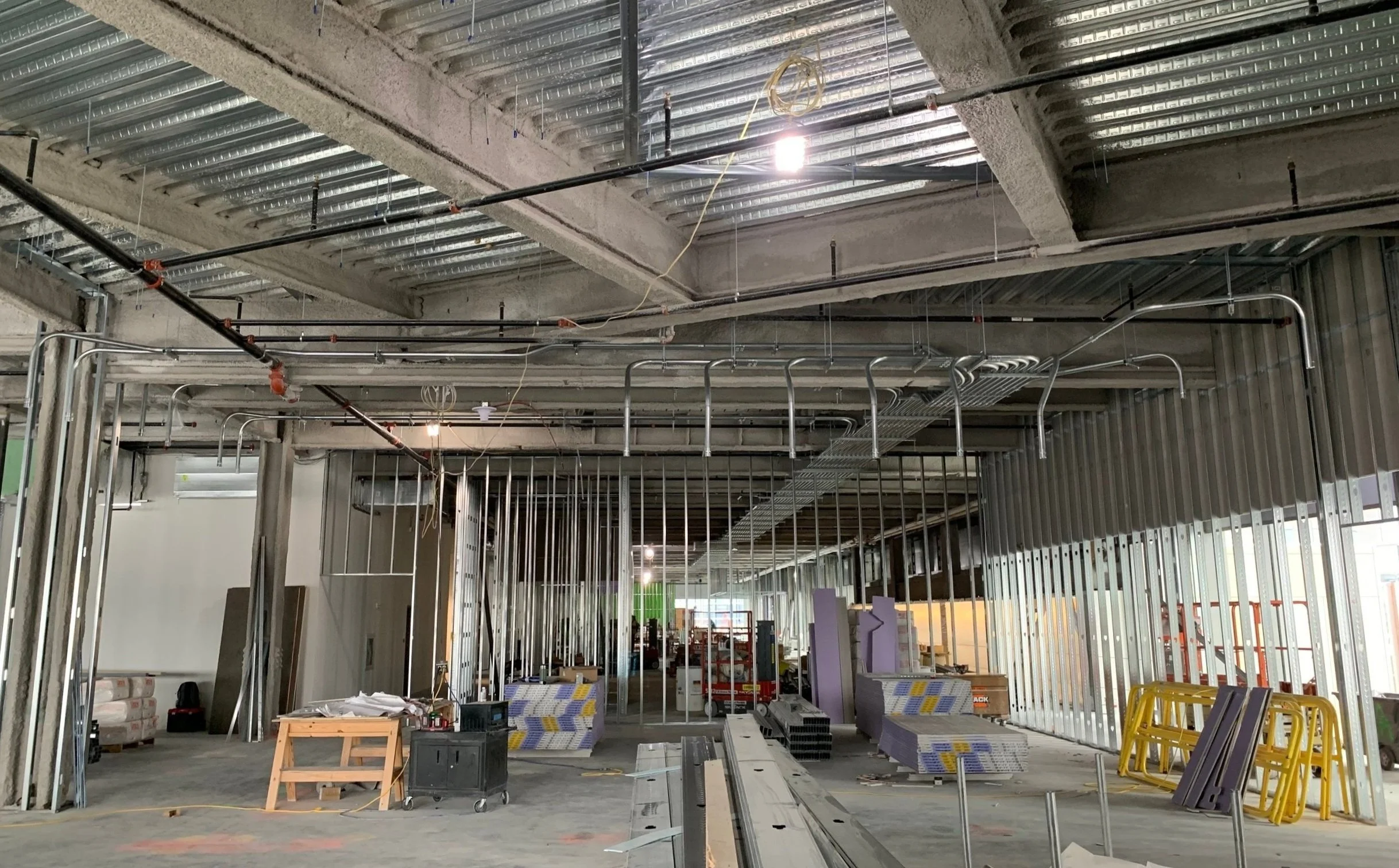 Construction site with exposed metal framing, electrical conduits, and unfinished walls inside a building.