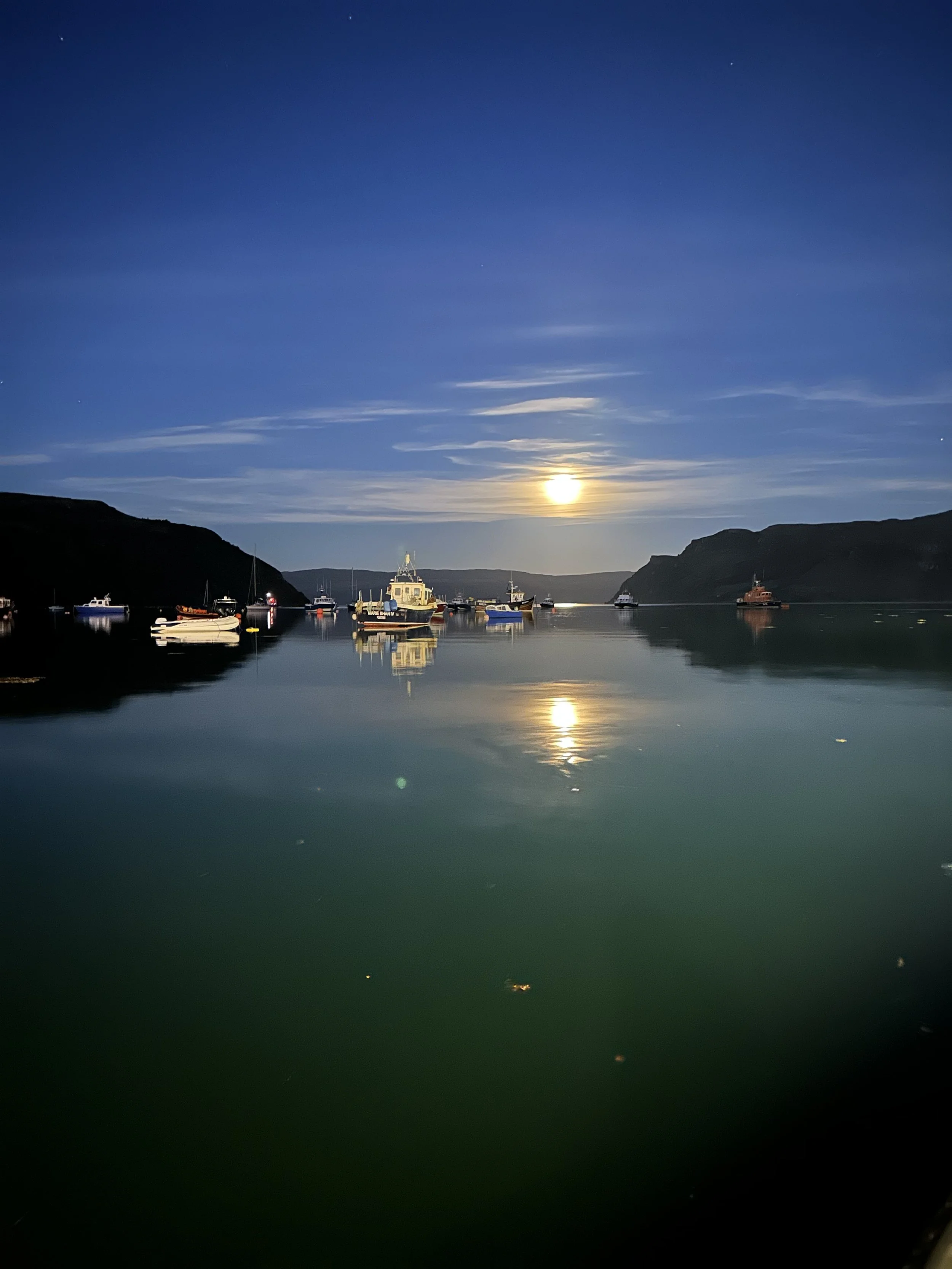 The harbor of Portree at night with the moon reflecting in the sea. Represents the unique luxury accommodations and authentic inns vetted for the Scotland journey.