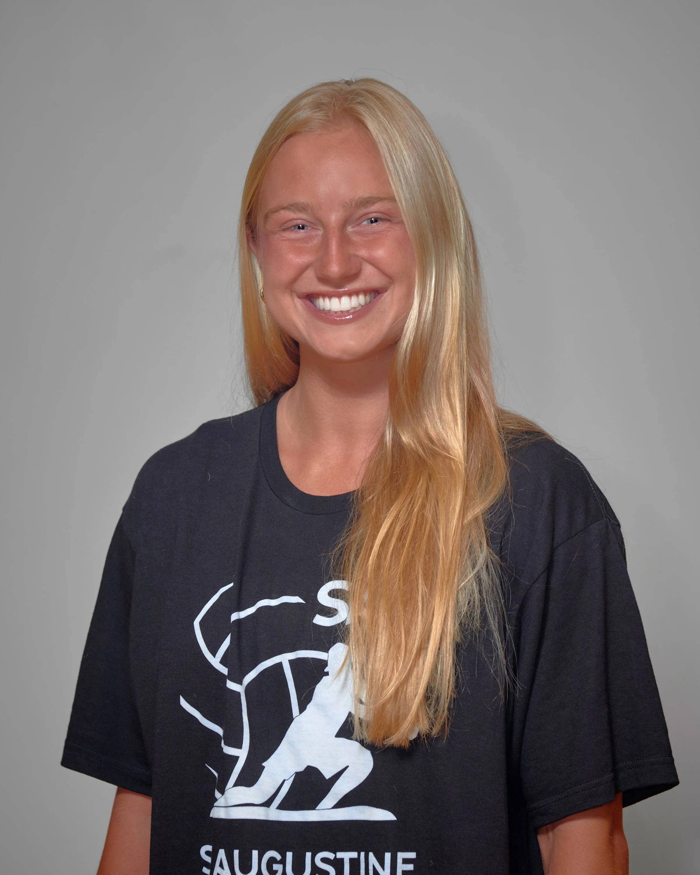 A young woman with long blonde hair, smiling and standing in a confident pose, wearing a black sports jersey with the number 0, and black shorts.