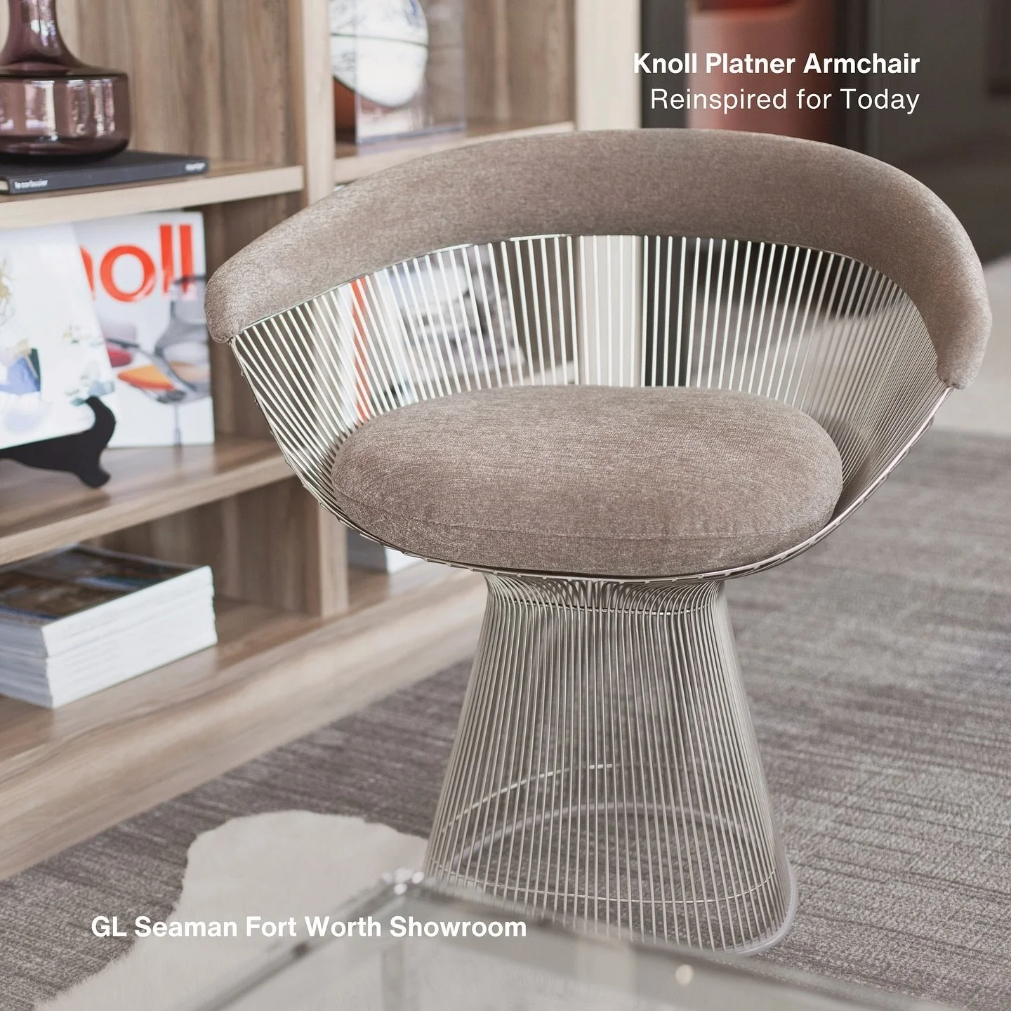 A modern, round, beige upholstered armchair with a metal wire frame and a matching base, situated in a furniture showroom with shelves, books, and decorative items in the background.
