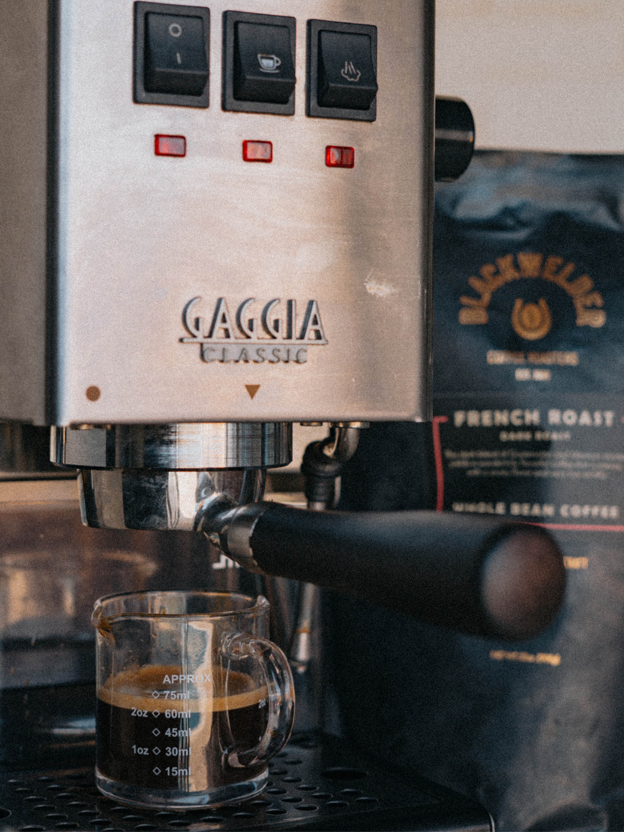 A close-up of an espresso machine with Gaggia Classic branding, preparing coffee into a glass measuring cup placed underneath the spout.