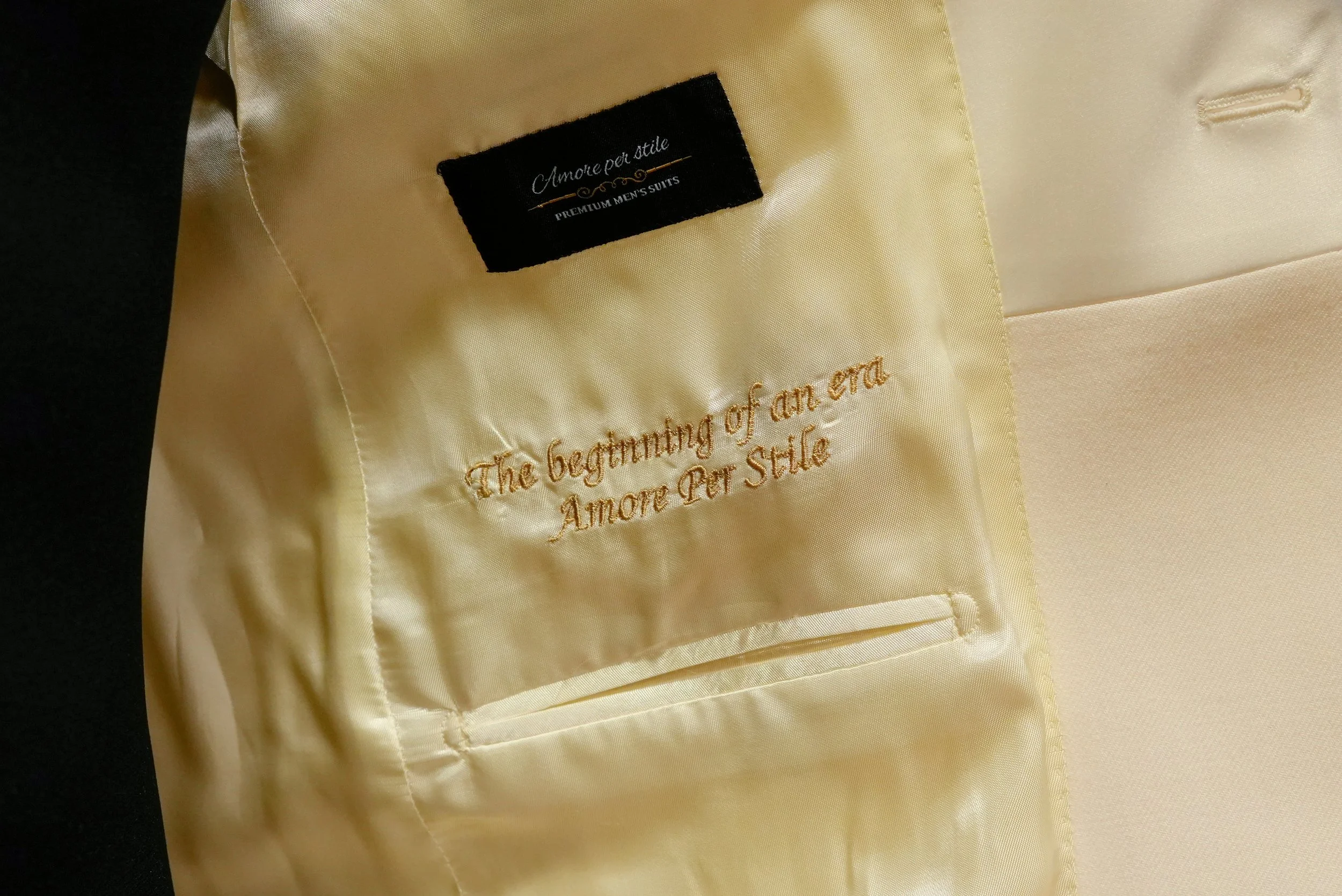 De binnenkant van een champagne kleurige trouwjas met goudgele borduursel dat zegt: 'The beginning of an era. Amore Per Stile'.