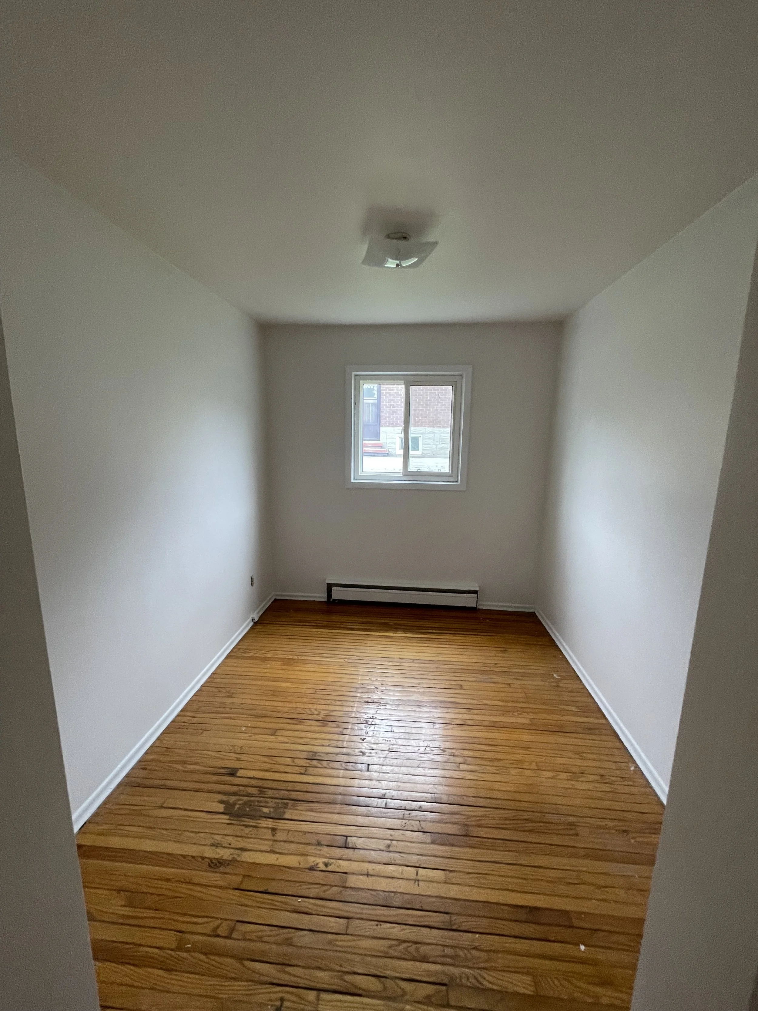 Empty small room with white walls, hardwood flooring, a window, and a ceiling light fixture.