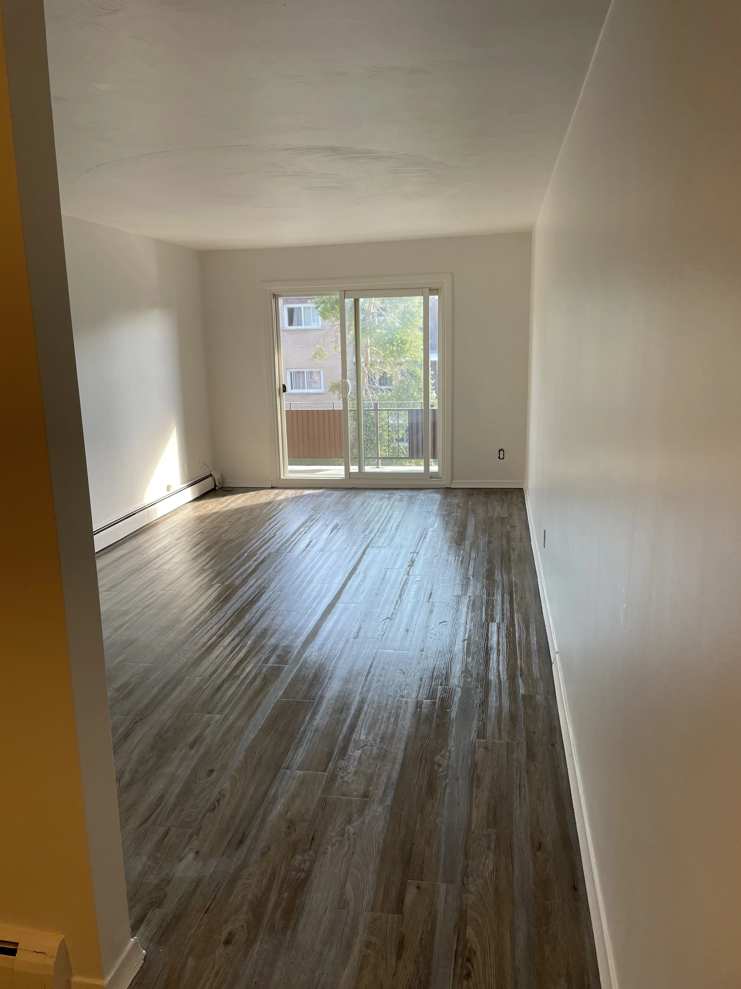 Empty room with wood flooring, white walls, and sliding glass door leading to a balcony.