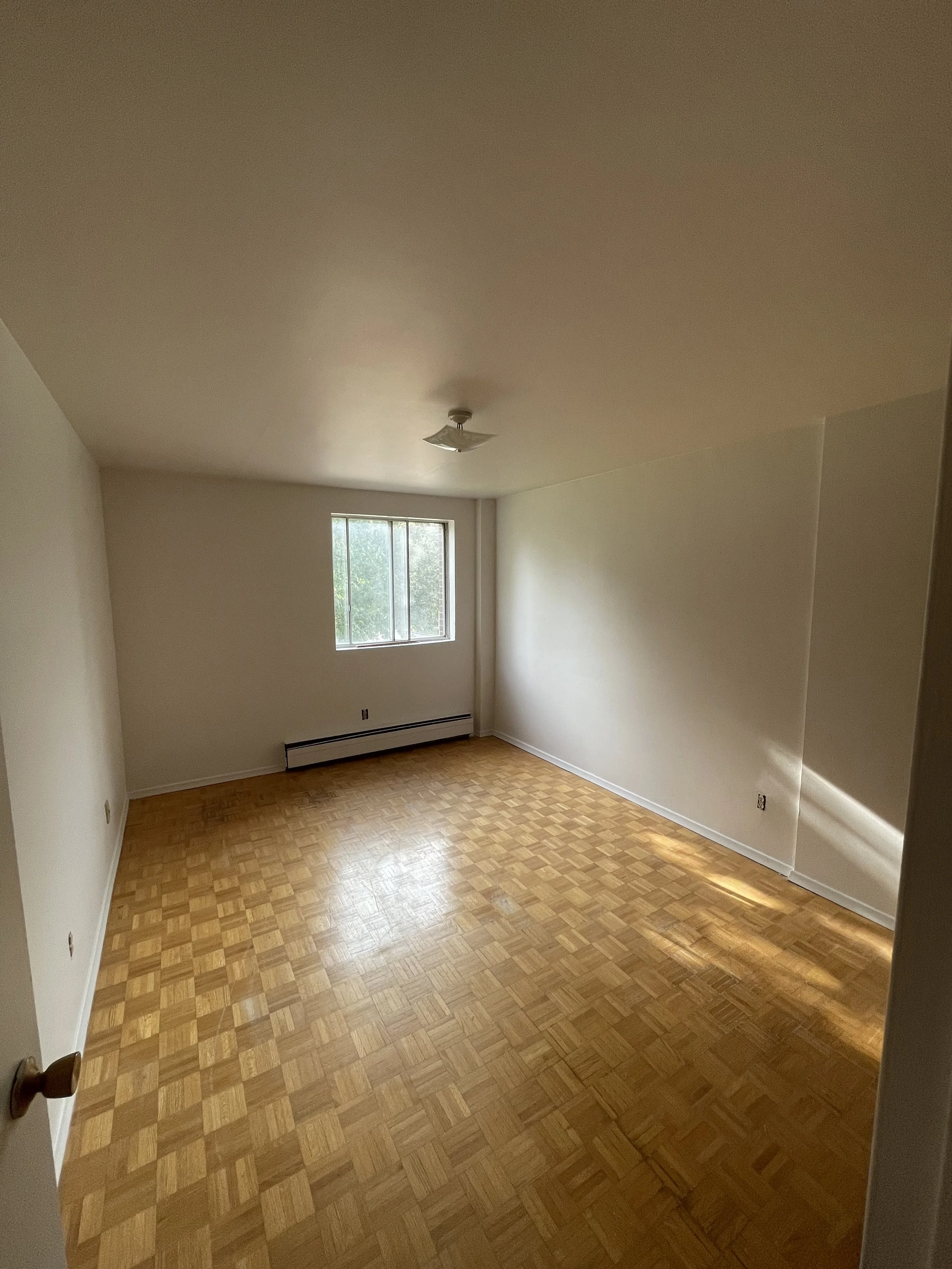 Empty room with hardwood flooring, white walls, a window, and a ceiling light fixture.