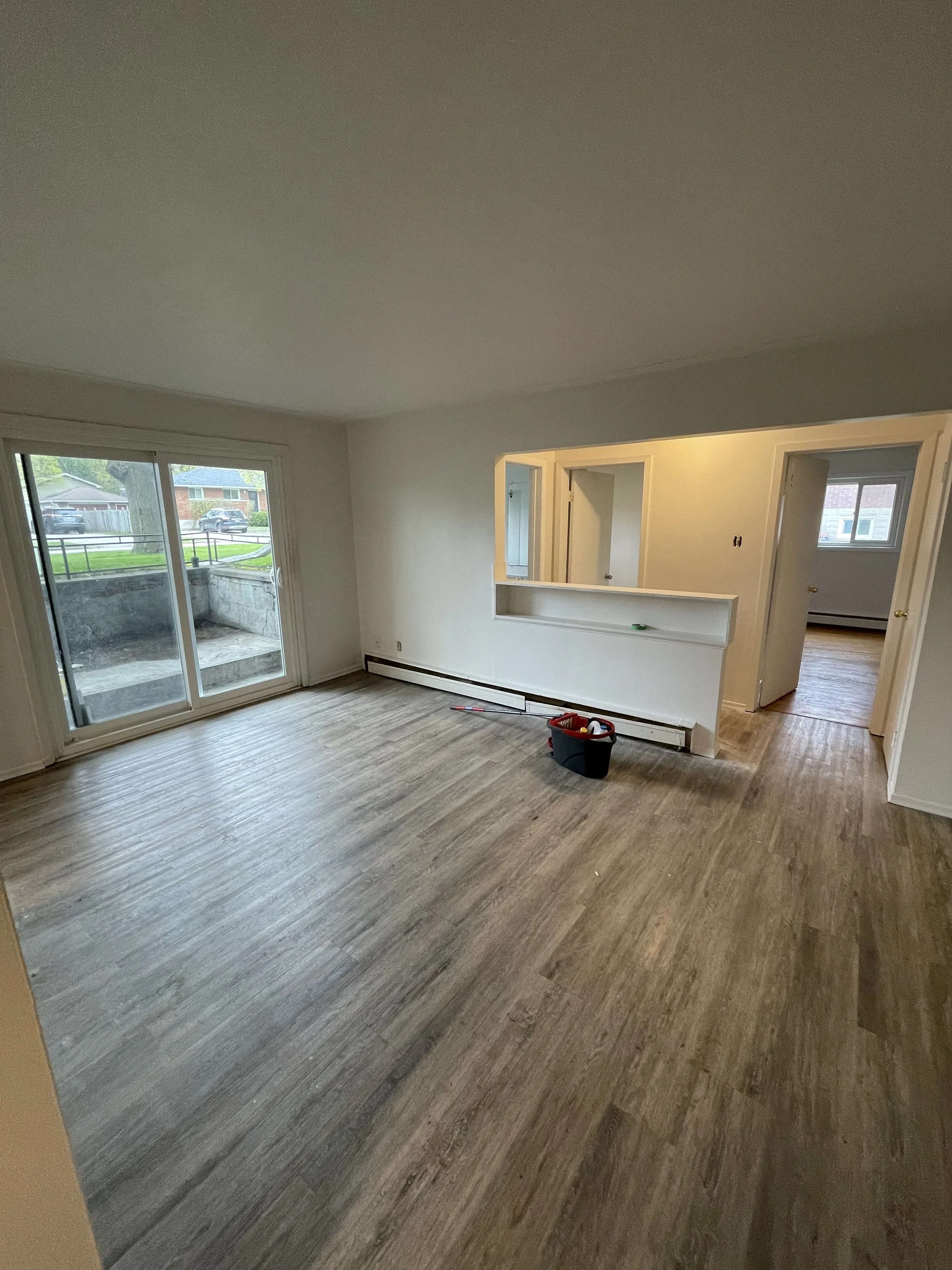 Empty living room with large glass sliding door, wood flooring, and an open view to an outdoor patio.