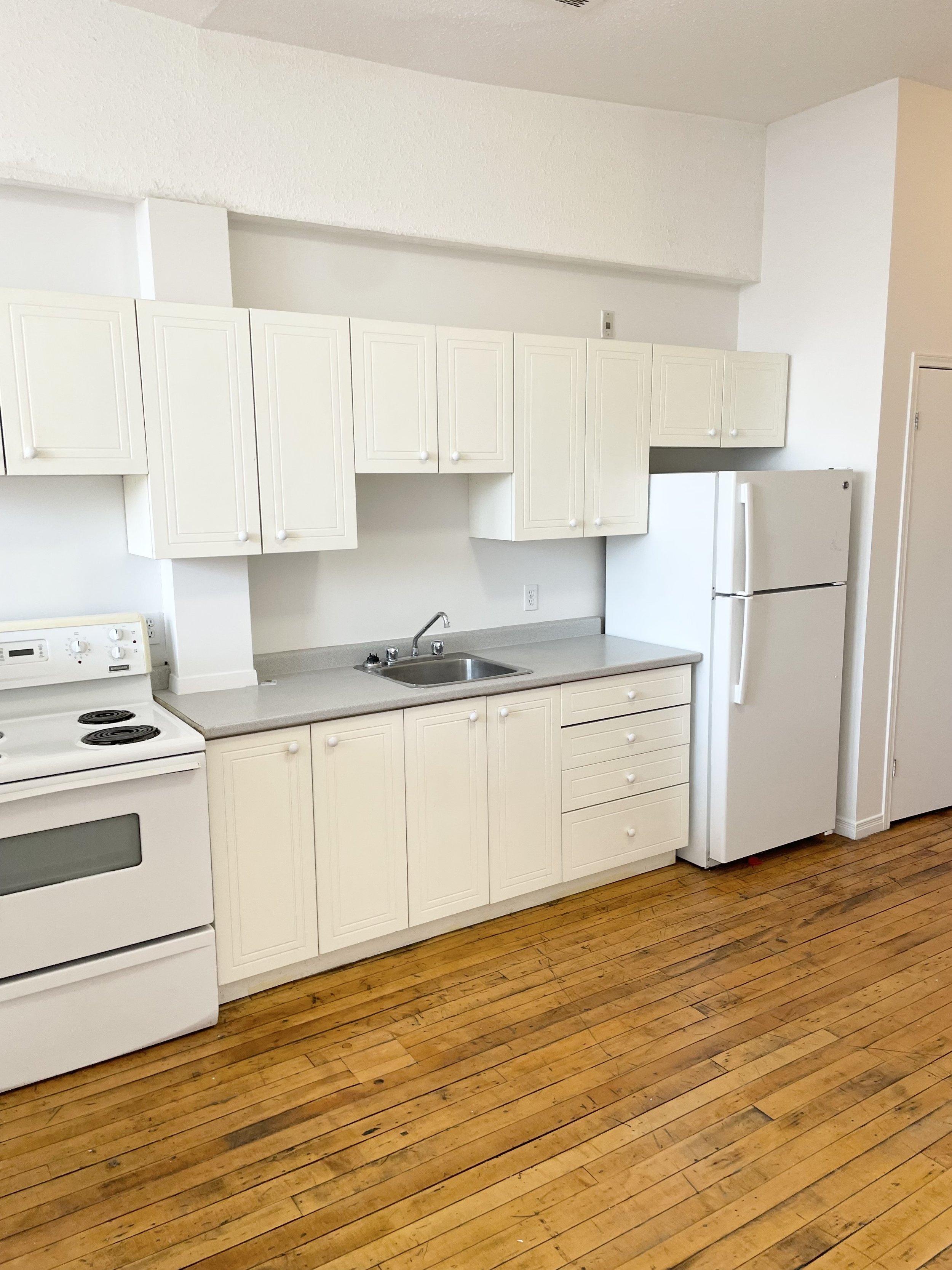 White kitchen with upper and lower cabinets, a sink, a refrigerator, and a stove, with a wooden floor.