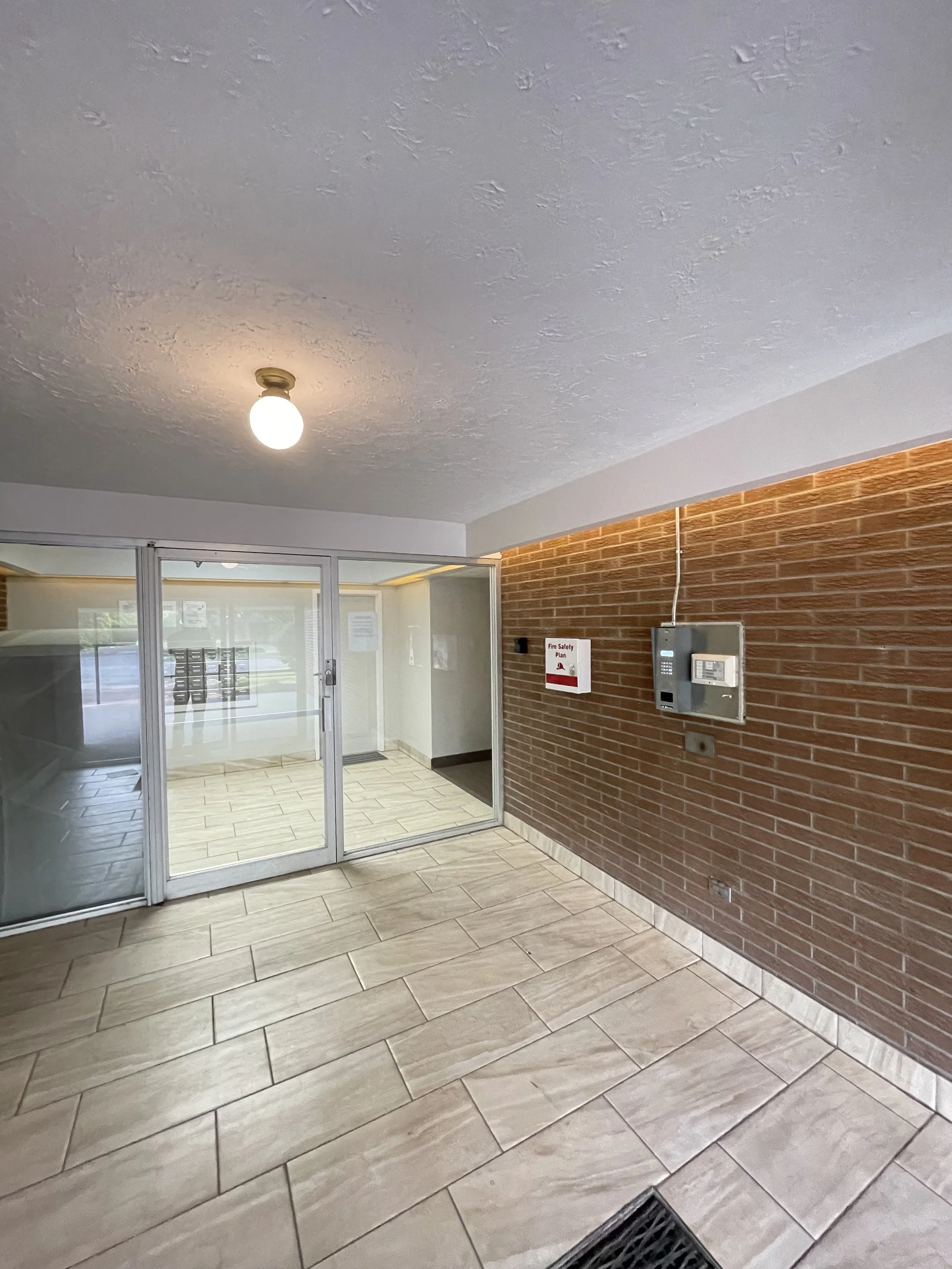Indoor lobby area with a brick wall, a security system panel, a fire safety plan, and glass doors leading outside.