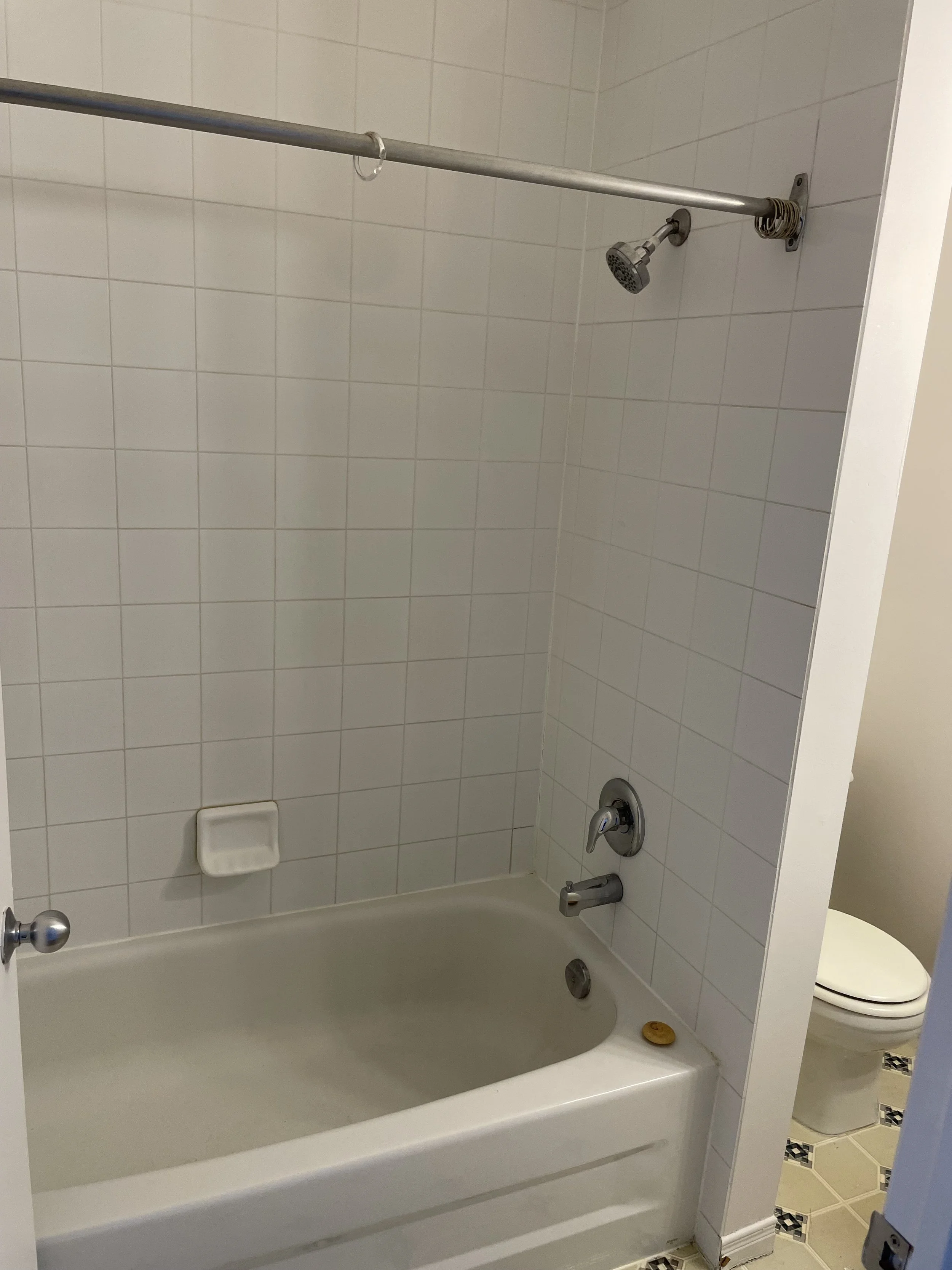 Bathroom with a bathtub, showerhead, soap dish, and a toilet visible behind a doorway.