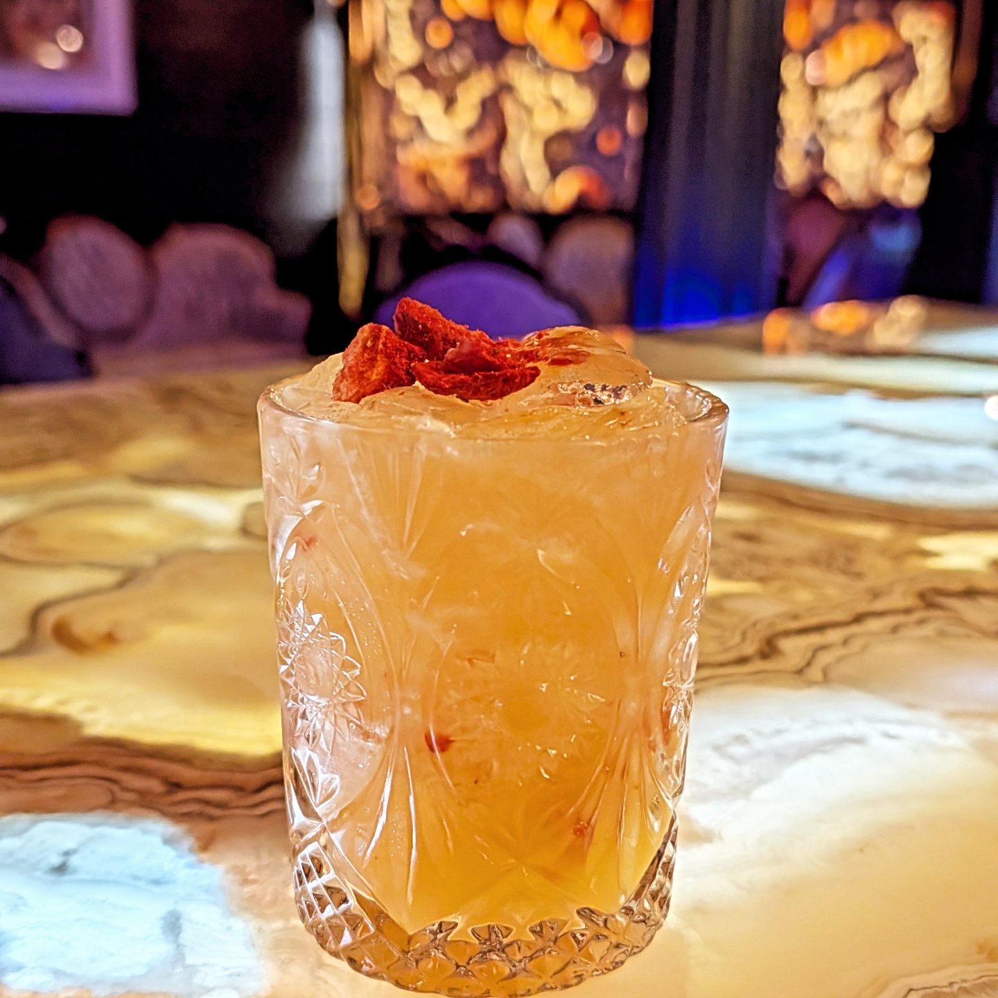A delicious hand-crafted cocktail in a textured glass garnished with dried fruit slices on top at Whisperz Speakeasy.