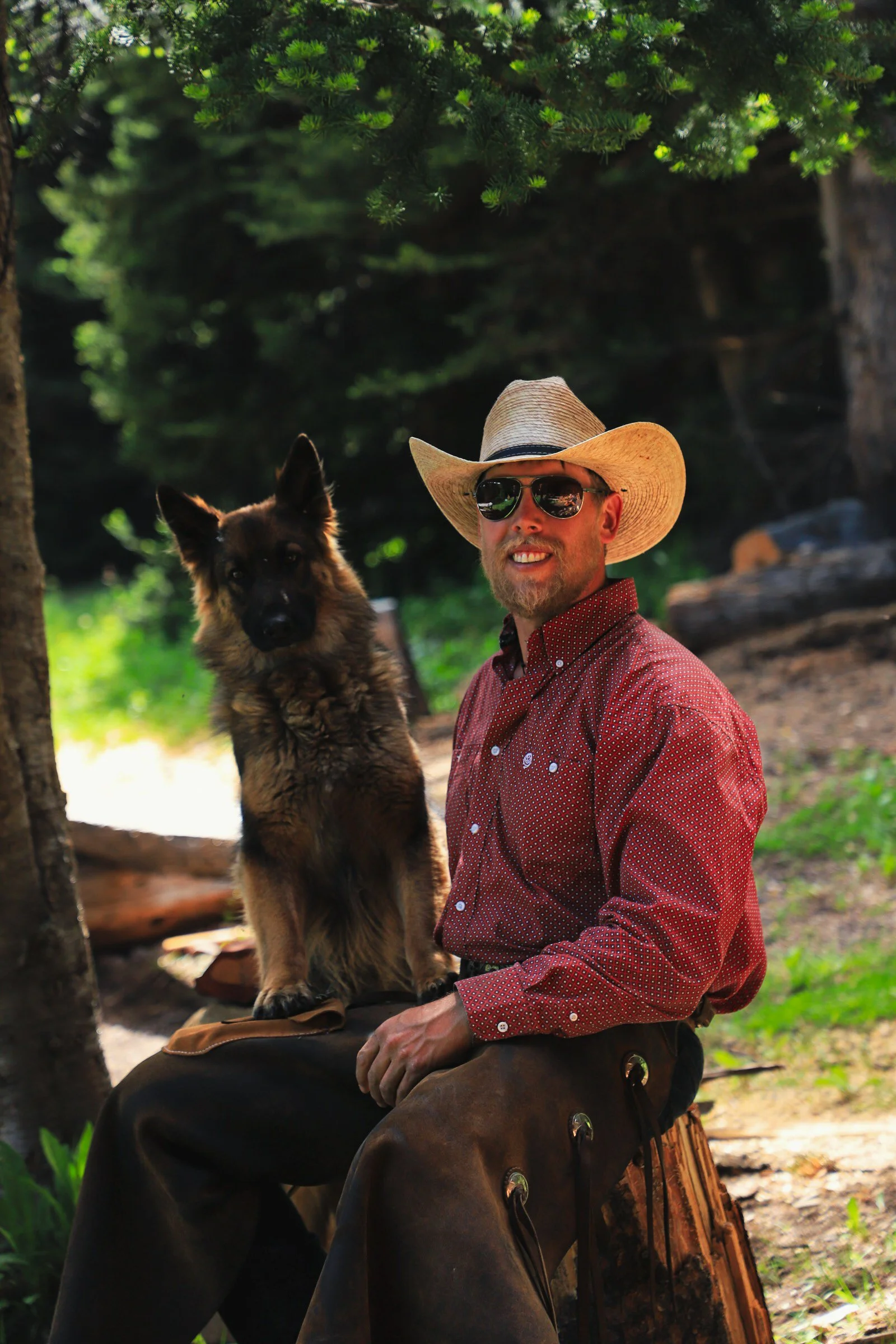 Aaron Bracewell with his Dog standing on a Meadow in the Mountains holding his Chain Saw