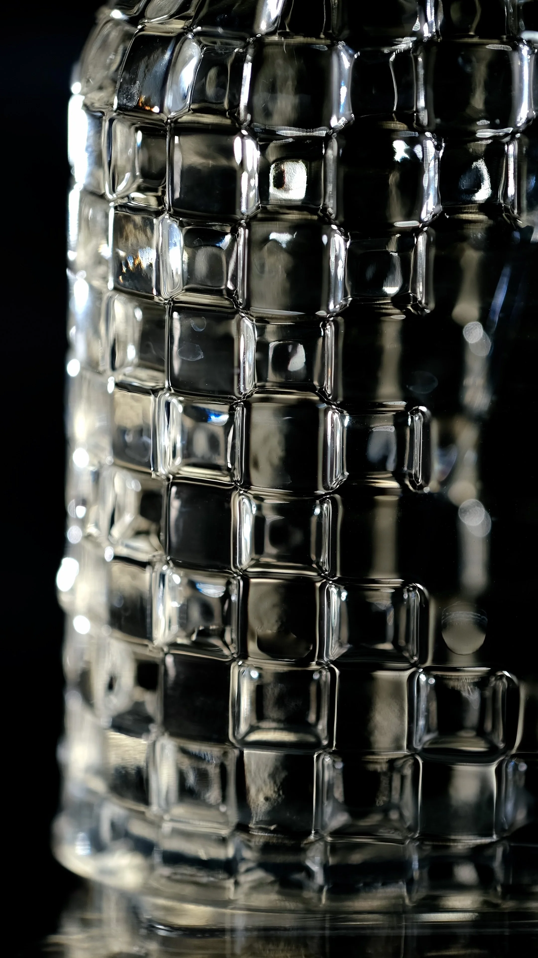 Verre en verre avec un motif en relief de carrés, capturant la lumière sur ses surfaces.