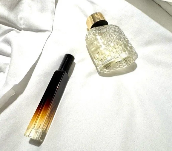 Un flacon 100ml de parfum en verre avec un bouchon doré, un vip sample format voyage 10ml, sur un lit d'hôtel Sofitel à Paris