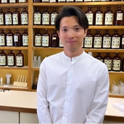 Parfumeur, Yusuke Masuda en blouse blanche devant un piano de parfumeur chez Galimard à Grasse