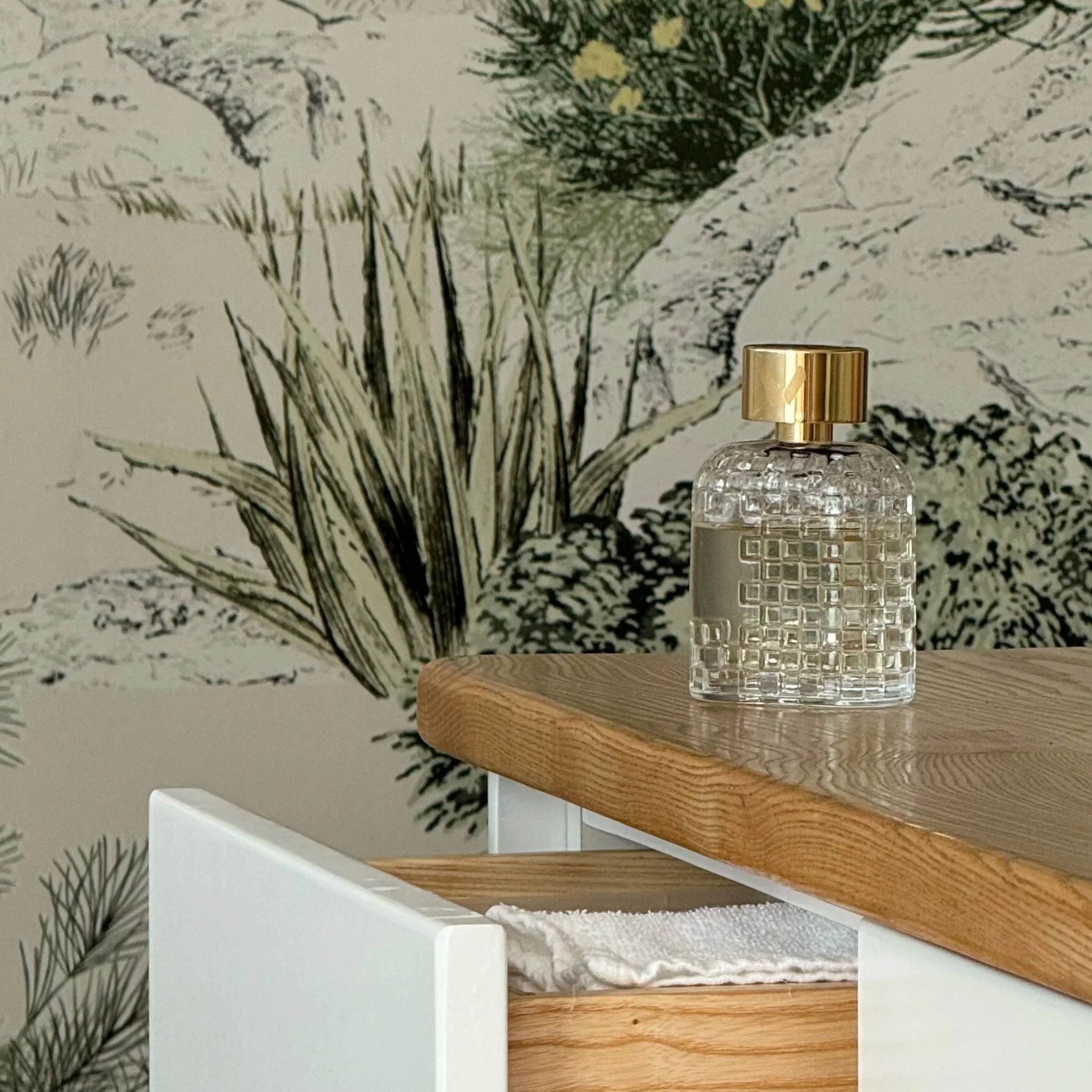 Décor intérieur d'un spa dans le sud de la France avec une bouteille en verre à motifs représentant l'eau de parfum Volanjara 100ml, un panneau en bois, une étagère en bois clair, un tableau en noir et blanc représentant des arbres