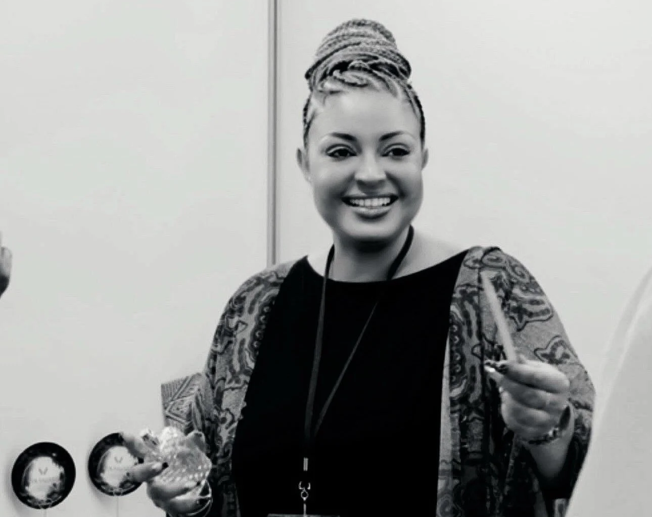Melle Vola VIGNY, créatrice et CEO de la marque de parfum Volanjara, souriante avec des cheveux coiffés en tresses en haut, vêtue d'un chemisier noir et d'une tunique Nanawax, tenant une mouillette, dans un environnement professionnel