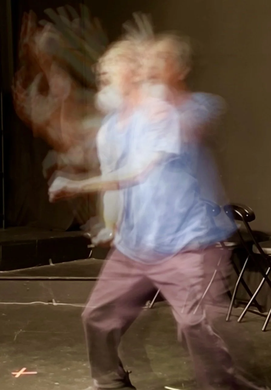 A blurry image that captures the many expressions and gestures of an actor with glasses, a white beard and light blue shirt performing in American Sign Language.