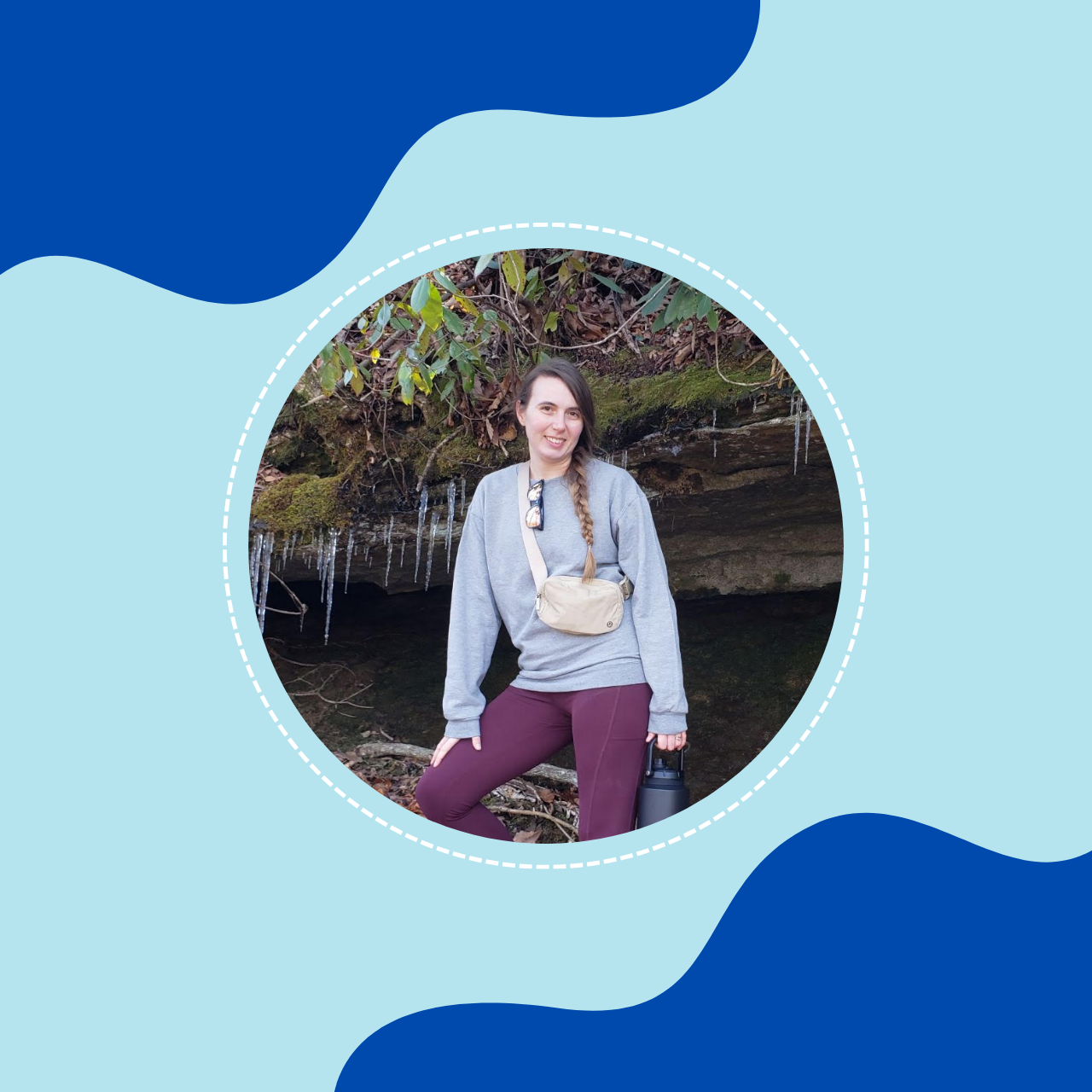 A woman with long braid, gray sweatshirt, maroon pants, standing outdoors in front of moss-covered rocks and icicles, holding a water bottle and small beige bag.