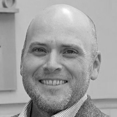 A smiling bald man with a beard, wearing a collared shirt and blazer.
