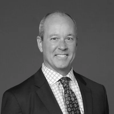 Black and white headshot of a smiling man in a suit and patterned tie.