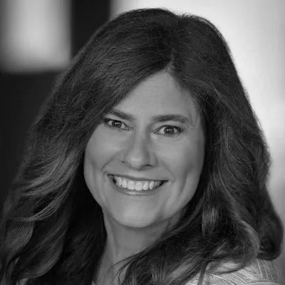 A smiling woman with long, wavy hair in a black and white portrait.