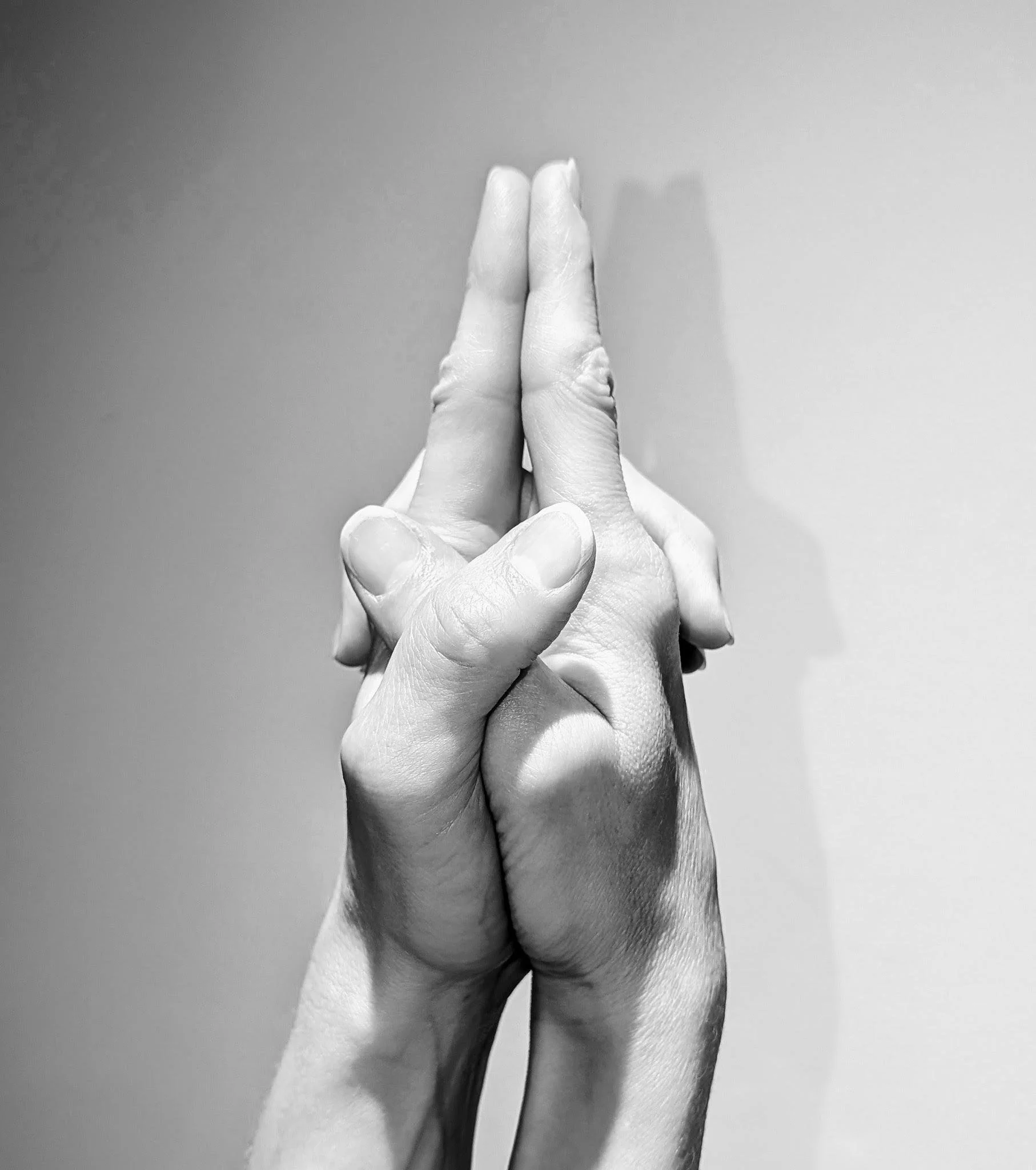 Close up black and white photo of hands in Ksepana Mudra, fingers interlaced with index fingers extended downward, a gesture of pouring out and letting go.