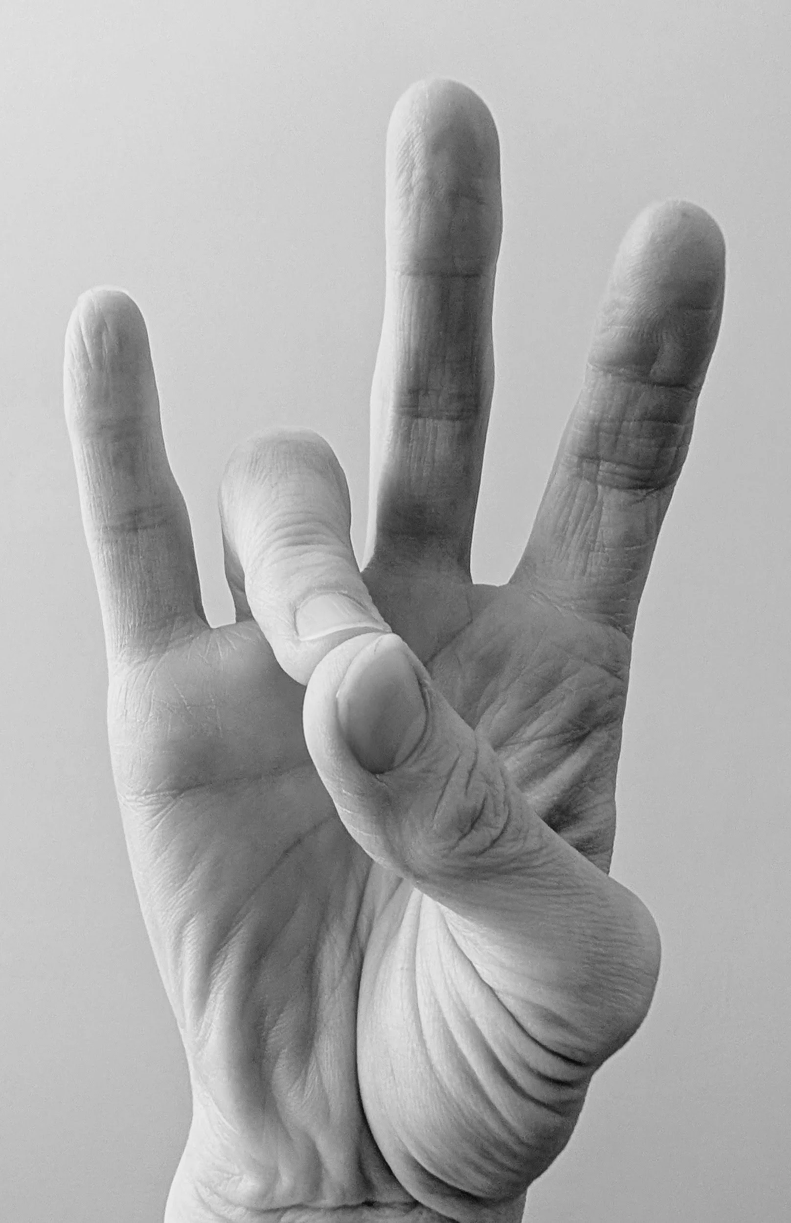 A close-up black and white photograph of a hand performing Prithvi Mudra (Earth Gesture), where the tip of the ring finger touches the tip of the thumb to increase the earth element and ground the body.