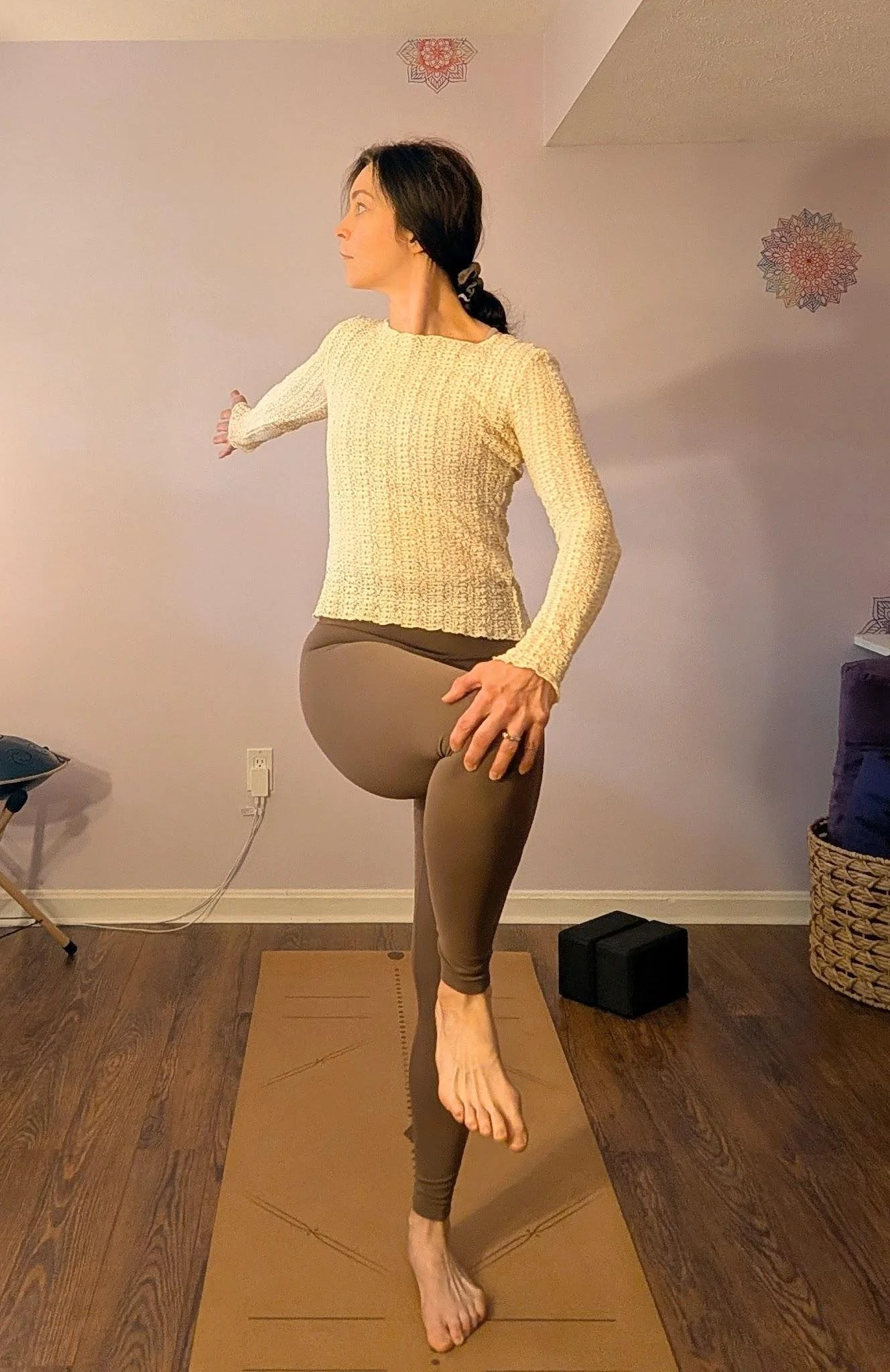 Woman in a standing spinal twist yoga pose, one hand resting on a raised knee, wringing out tension as summer transitions into fall.