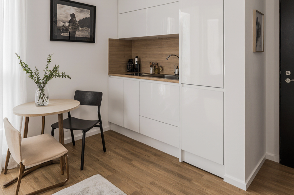 Salón moderno con sofá negro, mesa de madera y sillas, balcón con vista a la ciudad y plantas decorativas