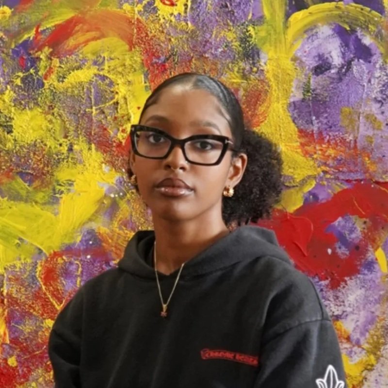 Portrait of Ryan Cosbert, conceptual artist and current BolsterArts Residency artist, standing in front of a colorful abstract painting.