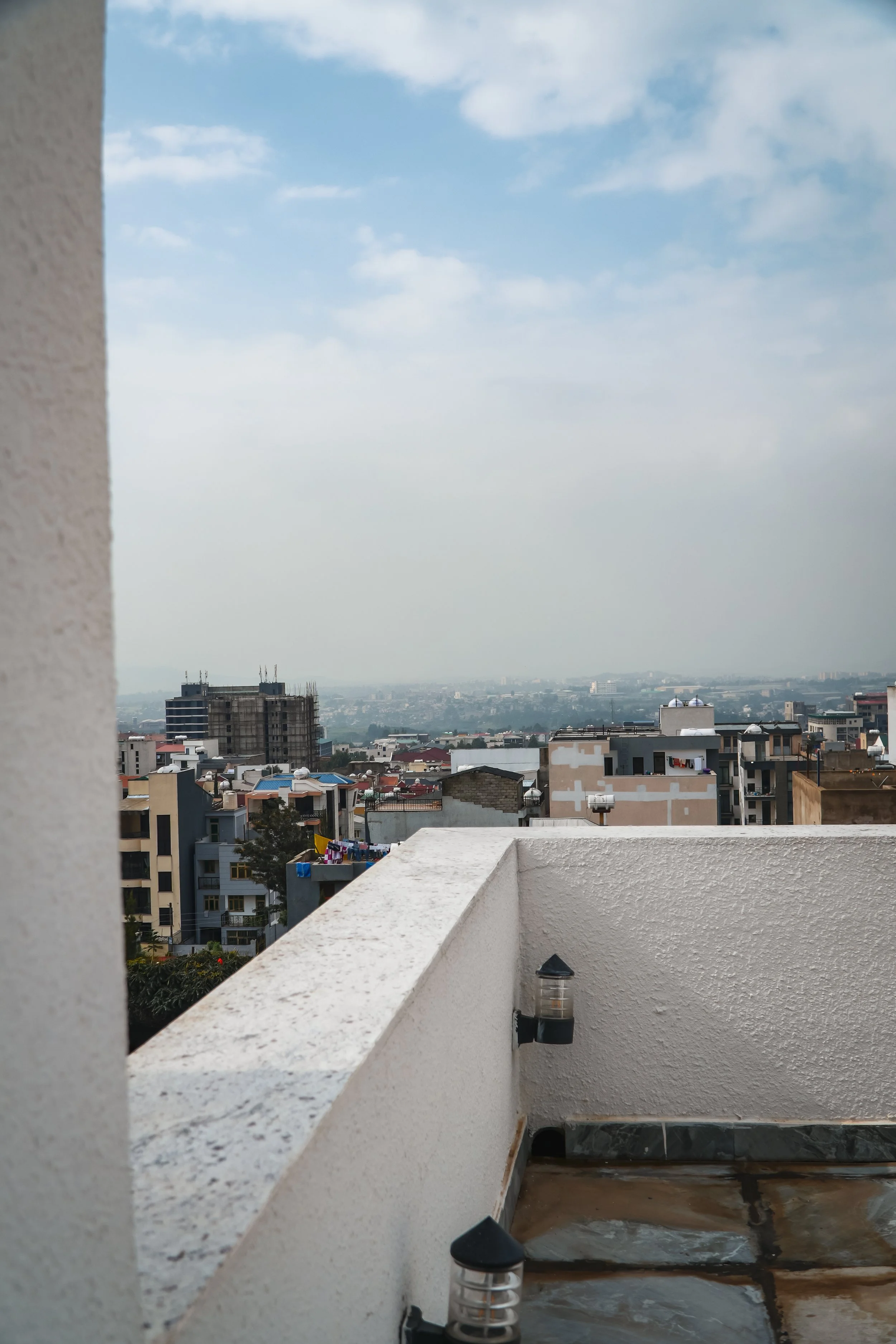 View from a balcony showing a cityscape with various buildings, some under construction, and a cloudy sky in the background.
