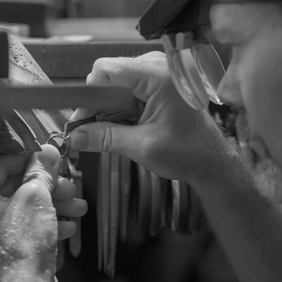 A person wearing safety goggles is working on a small mechanical device, using a tool with their right hand while holding the device with their left hand.