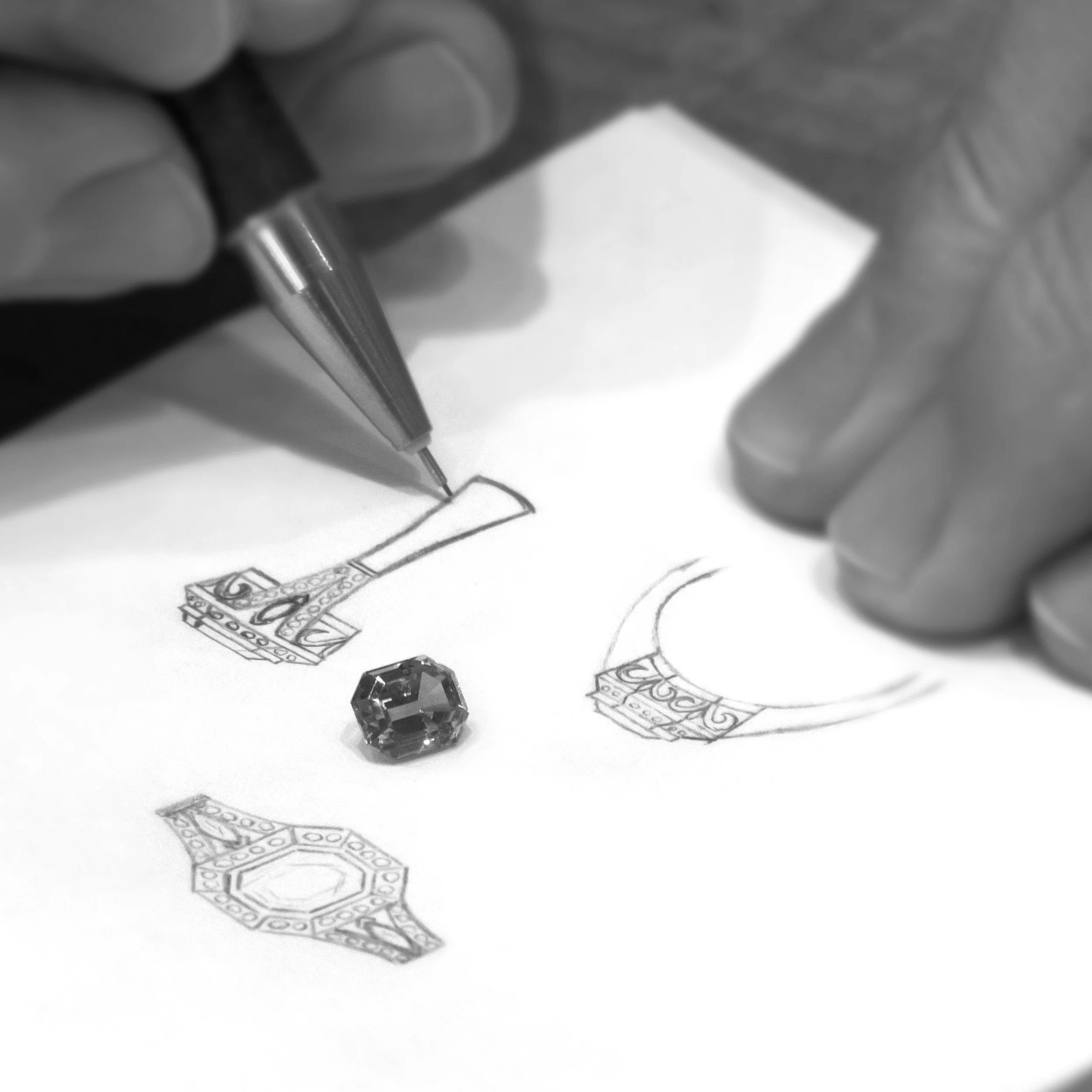 Person's hand drawing fashion sketches with a pen, with a gemstone on the paper.