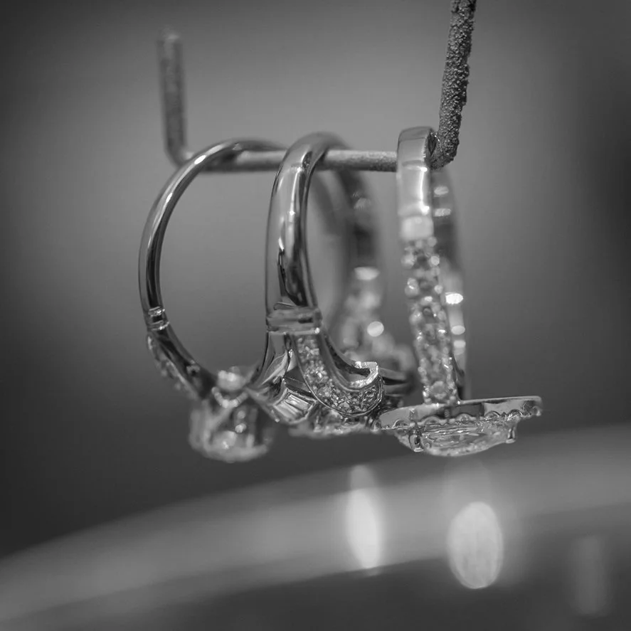 Close-up of three silver rings with diamonds hanging from a hook.