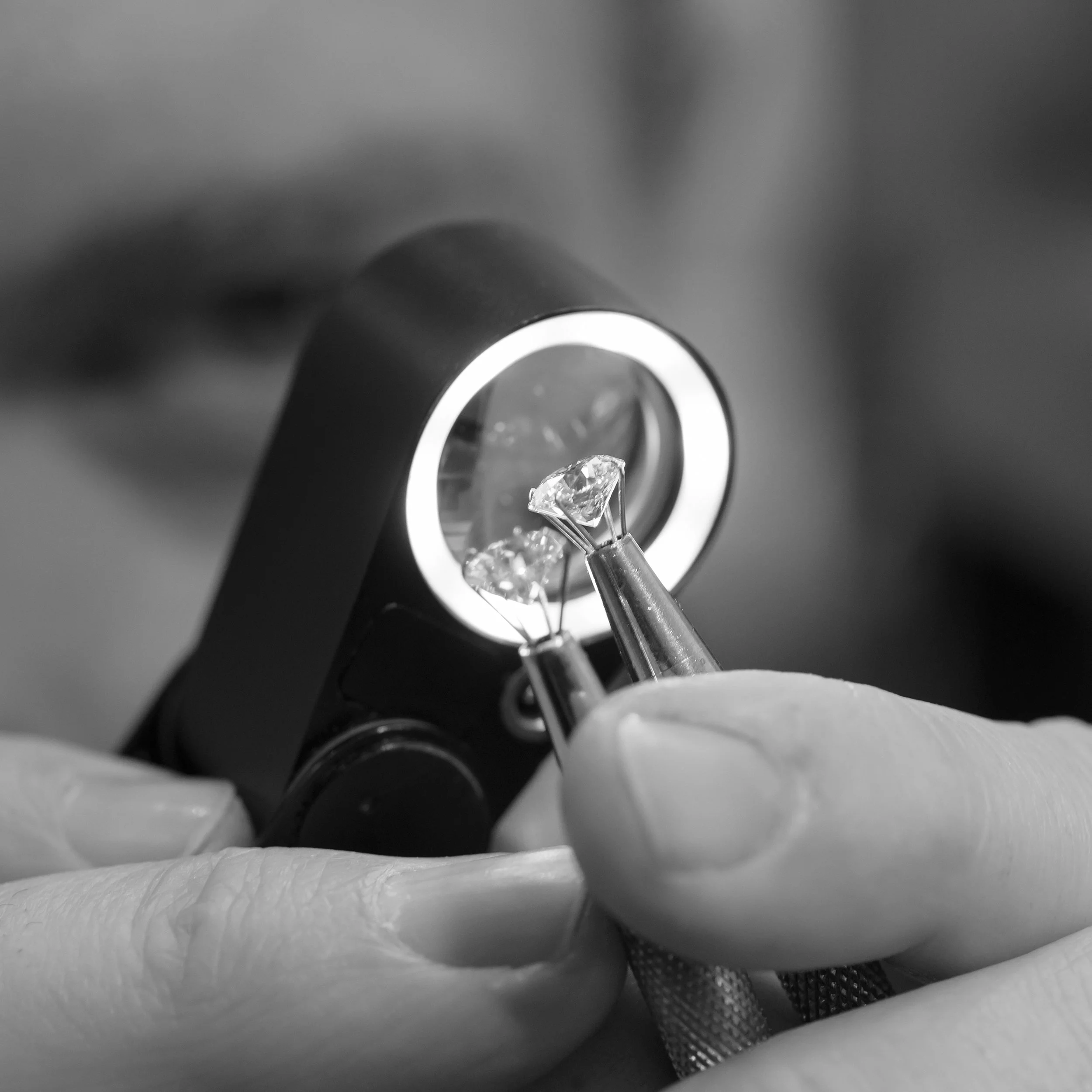 Close-up of a jeweler examining diamonds with a magnifying device and a pair of tweezers