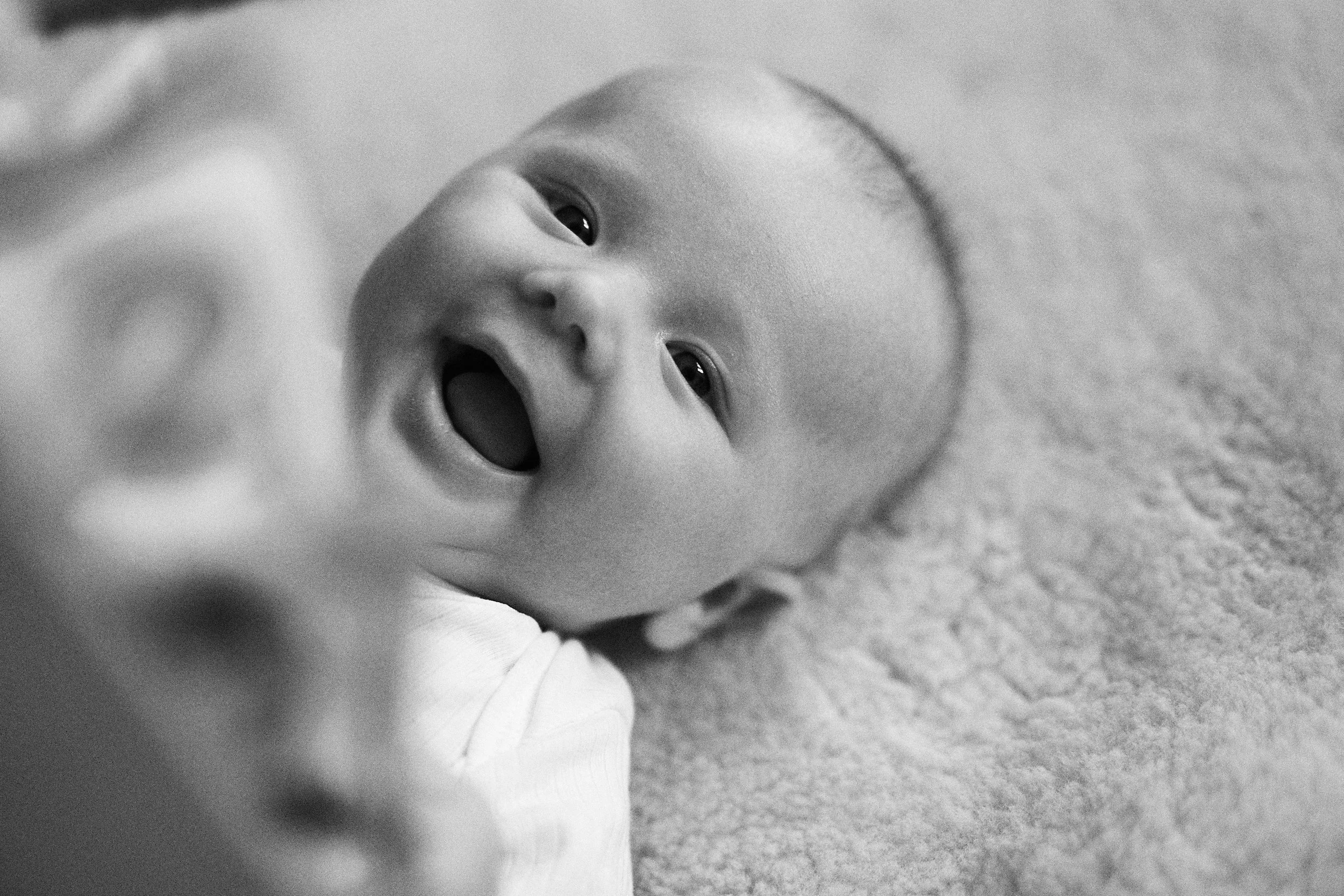 Black and white photo of a smiling baby lying on a soft surface.