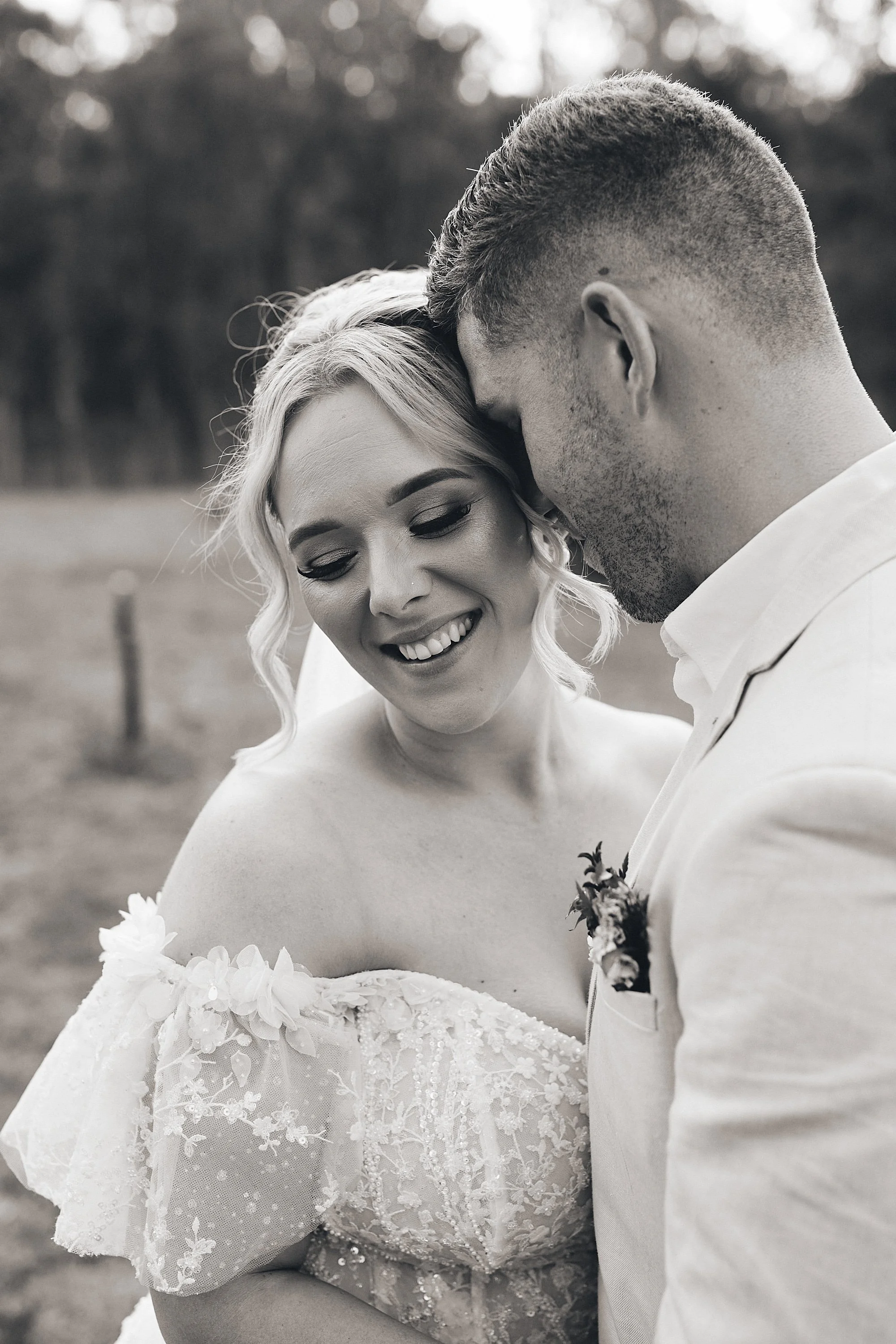 Bride and groom in a close embrace, smiling, during an outdoor wedding.