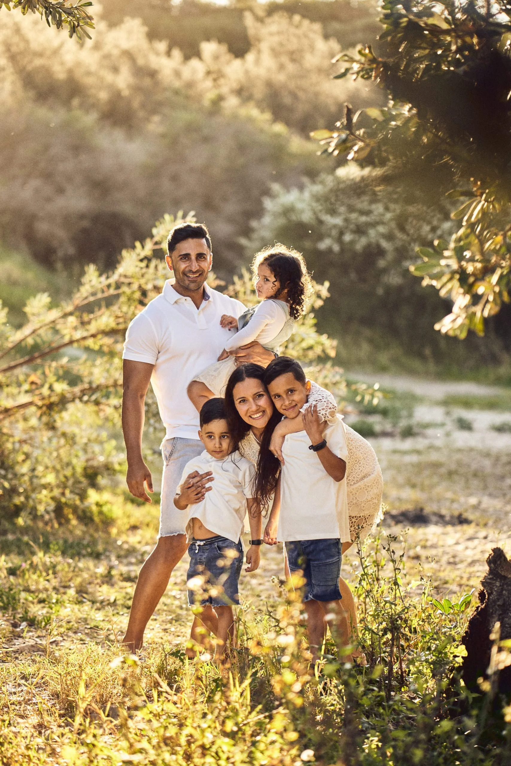 Family of five smiling outdoors in a sunny park.