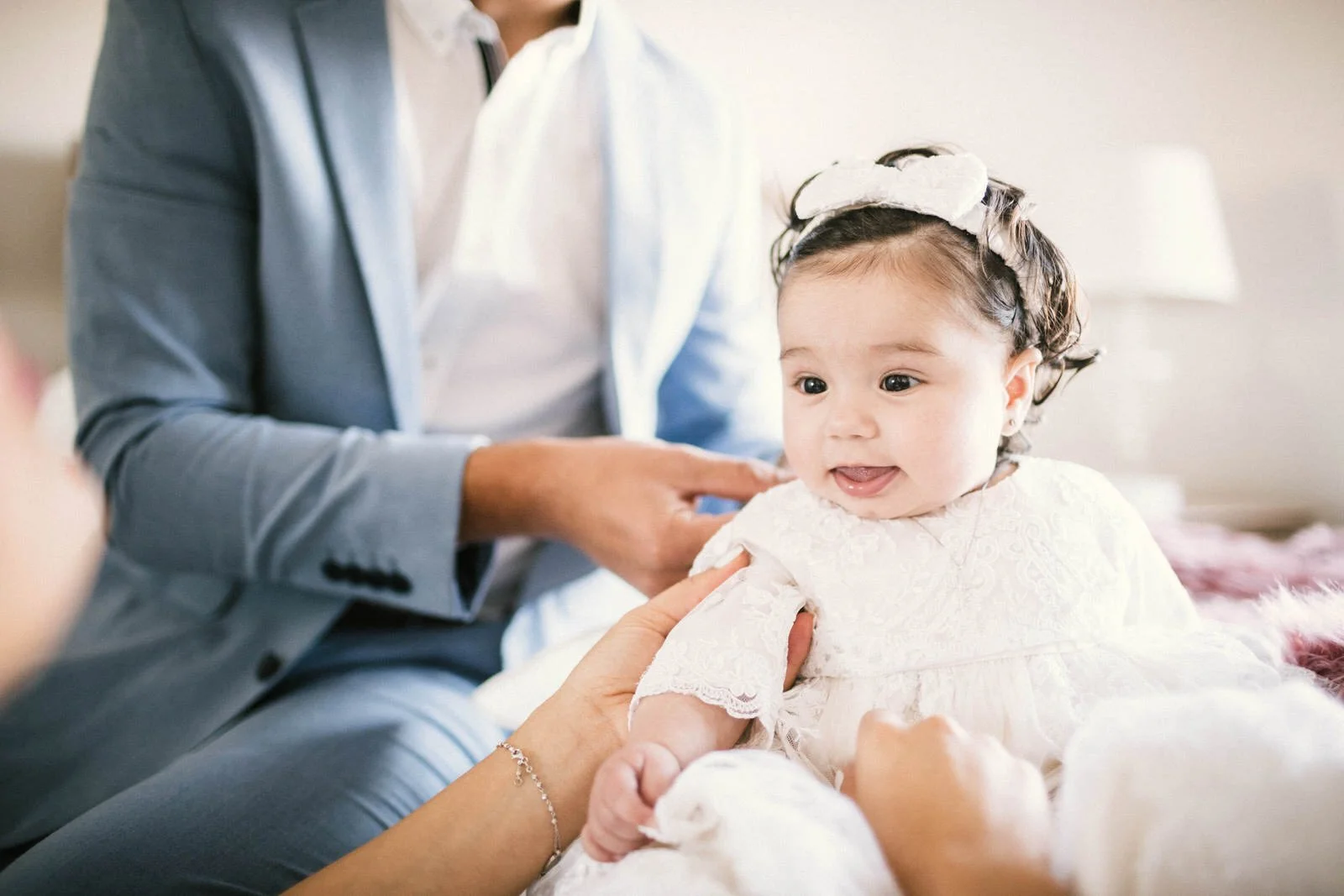 Baby in white dress being held by an adult