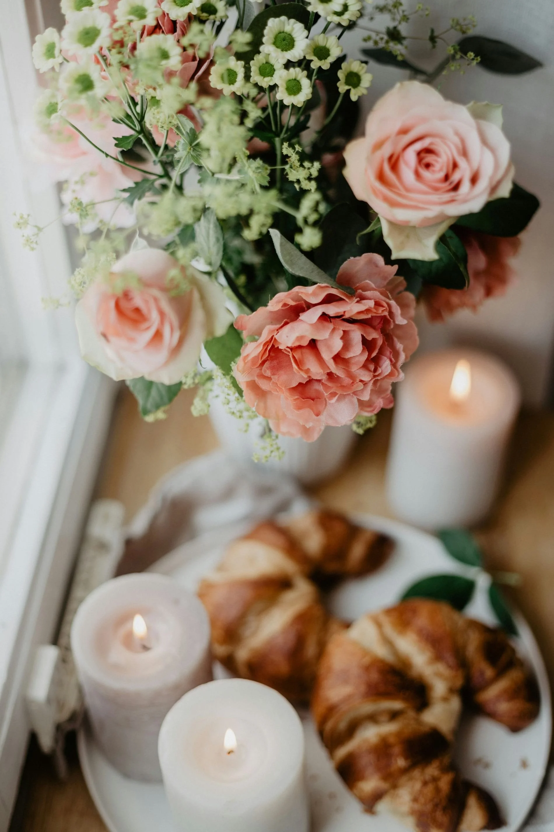 Flowers, candles and croissants next to a window