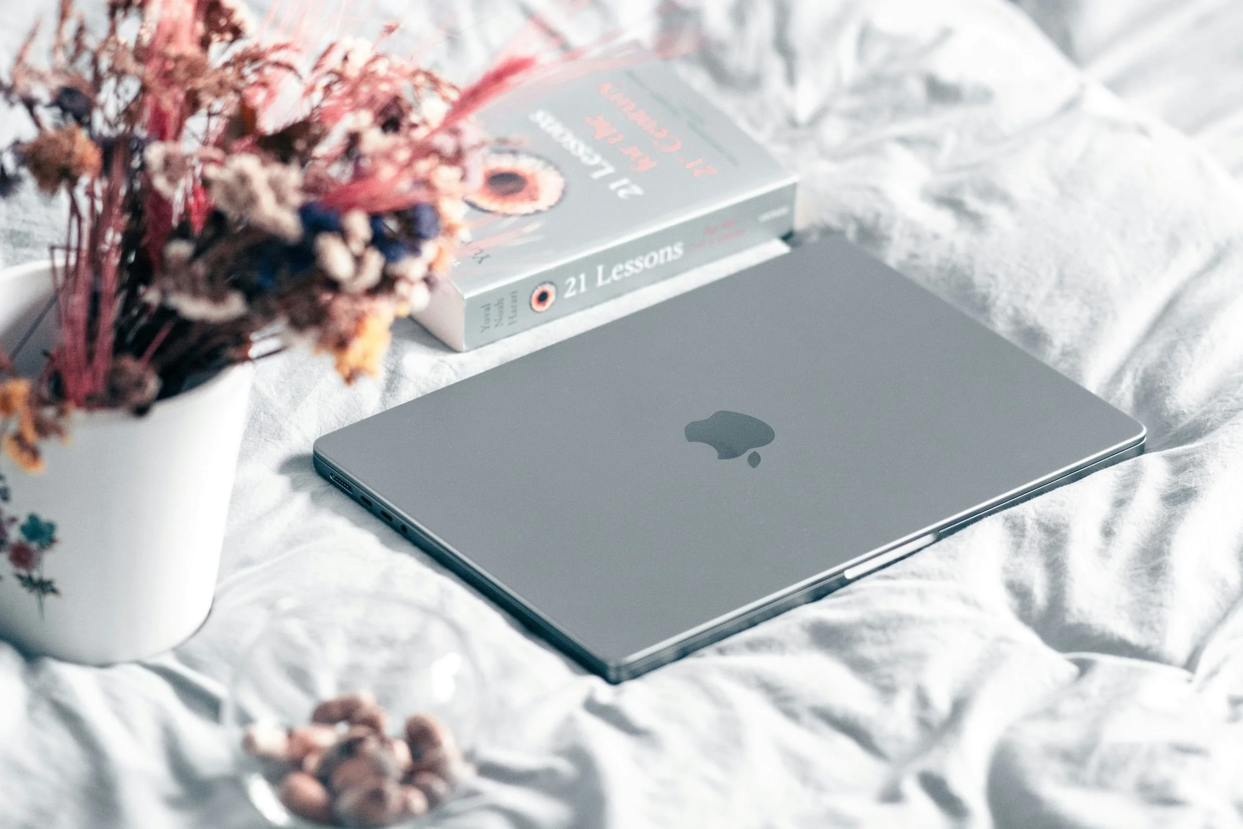 A wedding vendors laptop on a bed with a book and flowers
