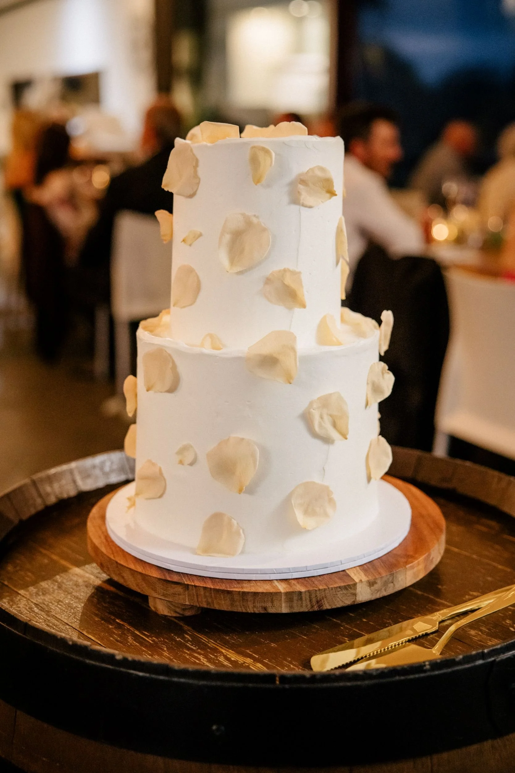 A butter cream wedding cake with rose petals displayed on a barrel at a wedding venue
