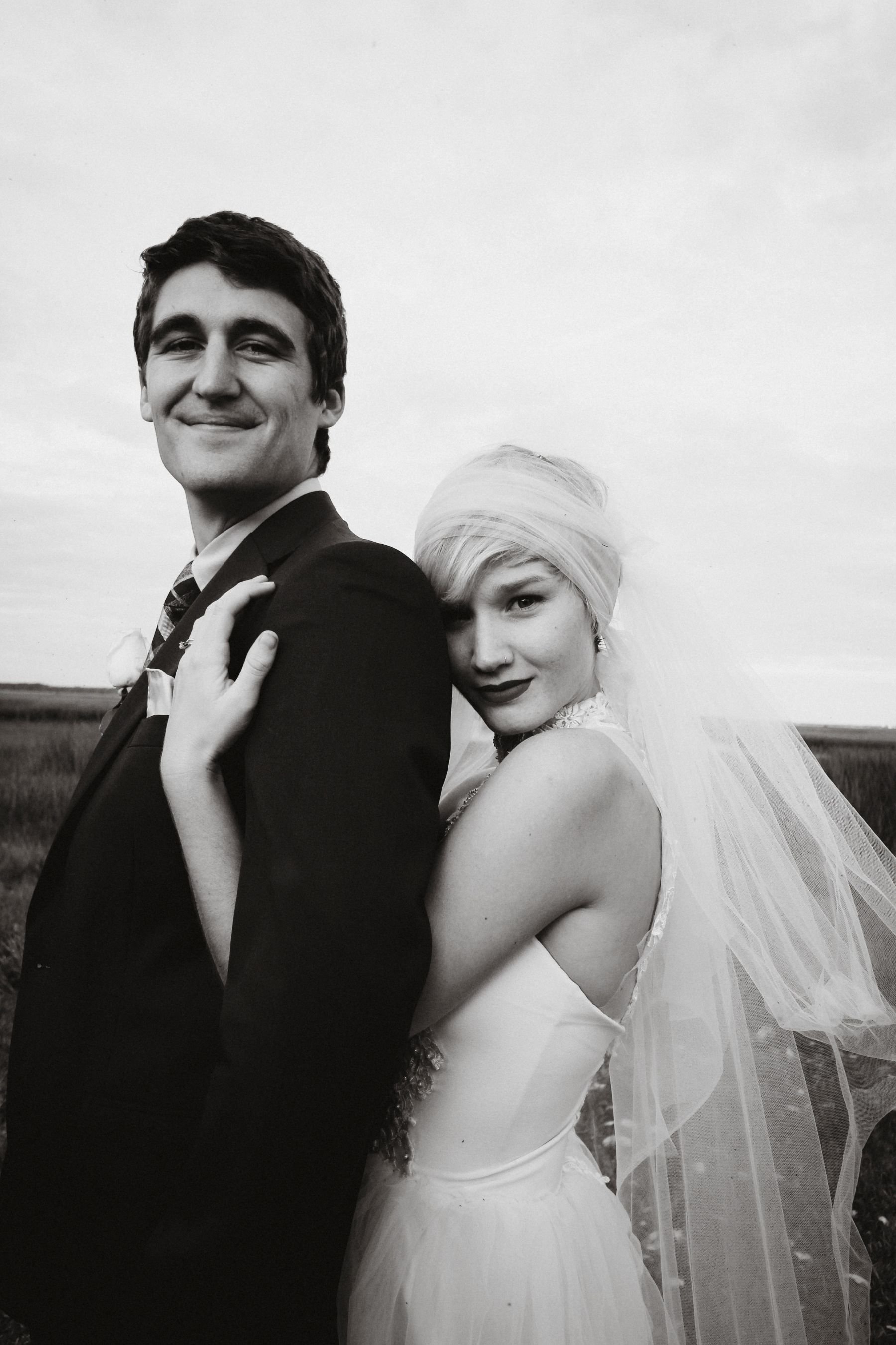 A wedding couple in vintage atire smiling and standing in a field