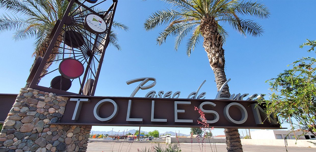 Entrance sign for Paseo de Lucres Tolleson with palm trees and blue sky in the background.