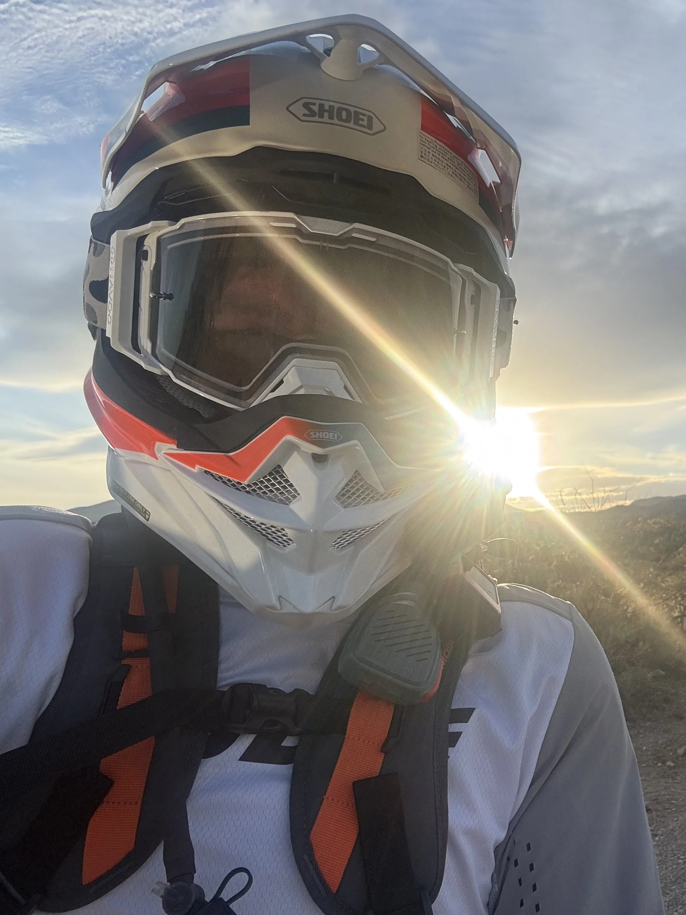 Shirtless man wearing a hat and glasses leaning against a motorcycle with bags. He has a tattoo on his arm and torso.