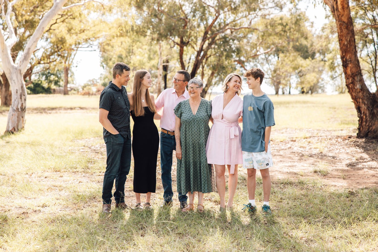 Family with teenage children and grandparents smiling at each other in a park