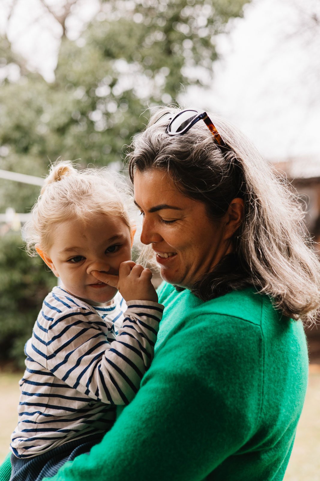 Woman holding toddler boy who is picking his nose