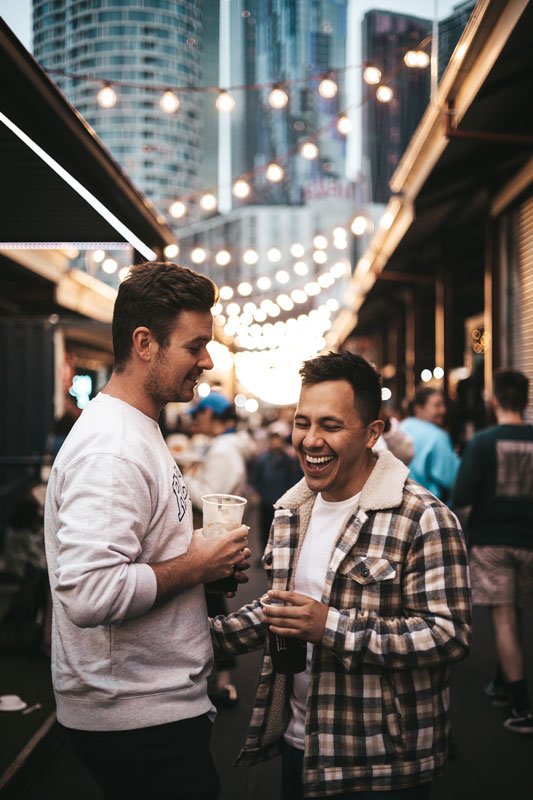 Young gay couple laughing at an outdoor marketing with a city skyline in the background